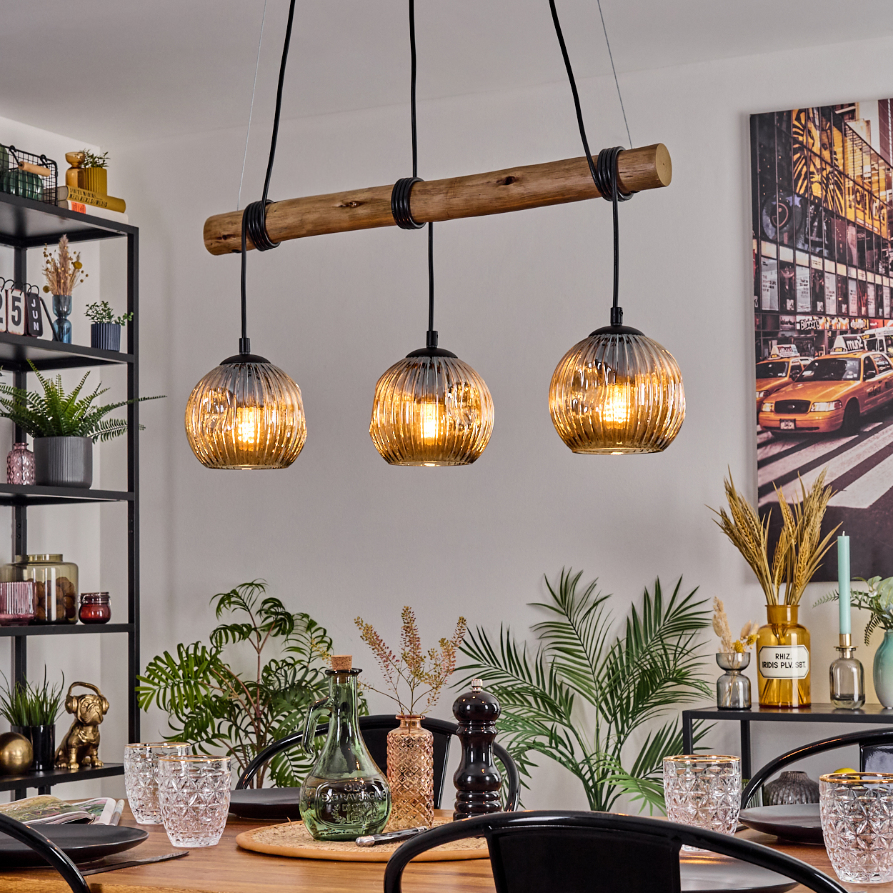 Esszimmer mit Holztisch, drei Pendelleuchten, Pflanzen, Gläsern und einem New York City Foto an der Wand.