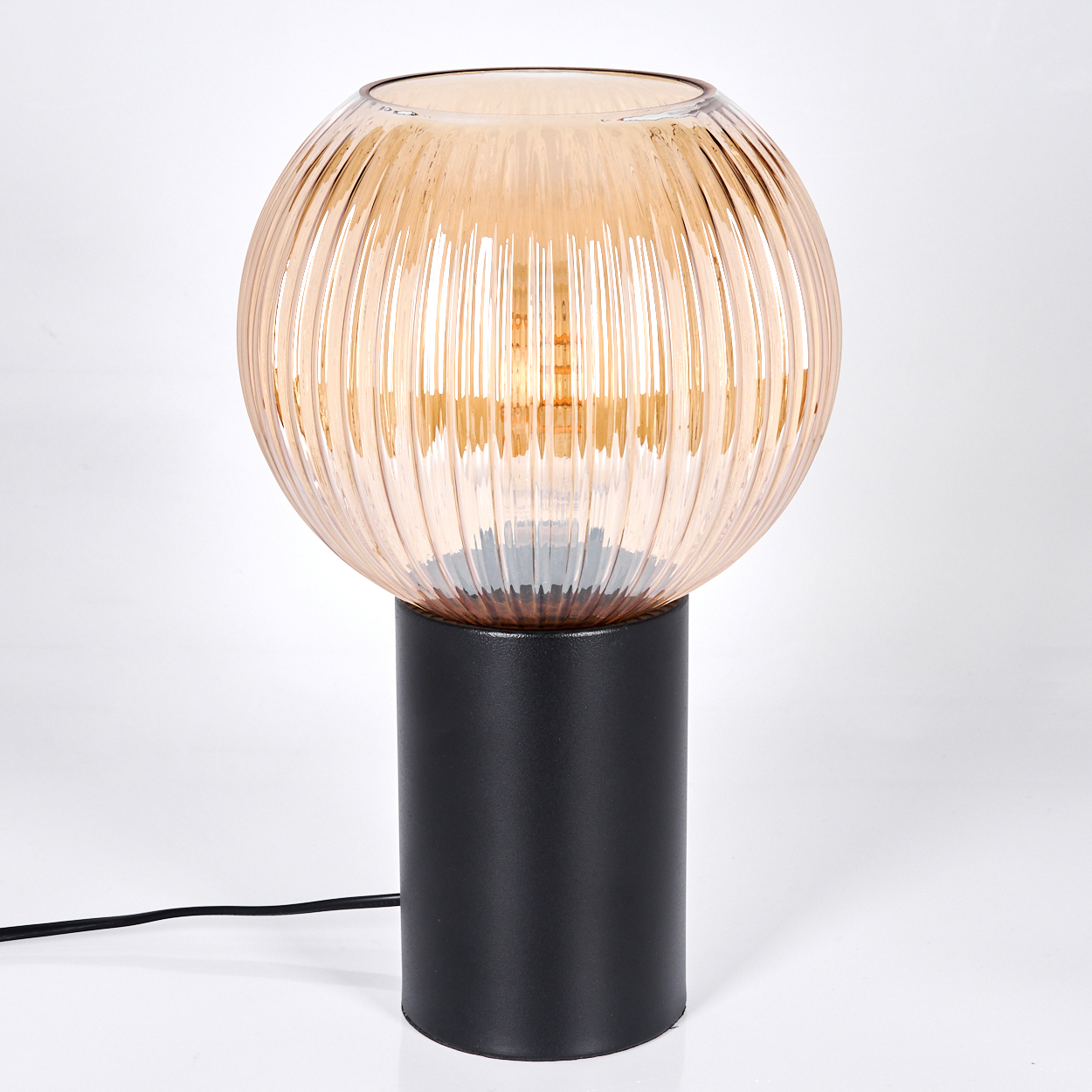 Eine Tischlampe mit einem kugelförmigen, bernsteinfarbenen Glasschirm, geripptem Design, auf einem schwarzen zylindrischen Sockel. Ein Netzkabel verläuft vom Sockel.
