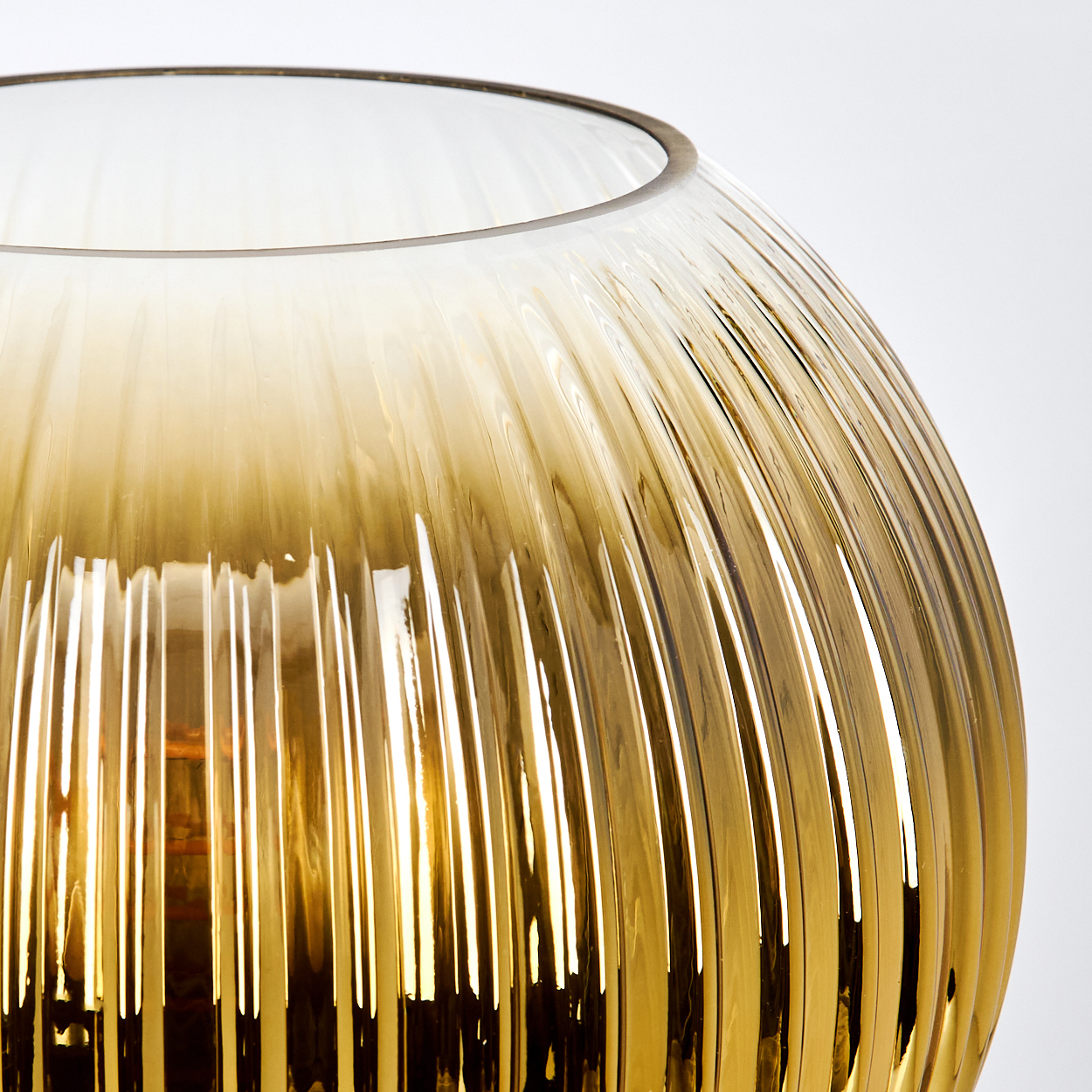 Nahaufnahme einer gerippten, bernsteinfarbenen Glasvase. Die Vase hat eine weite Öffnung und steht vor weißem Hintergrund.
