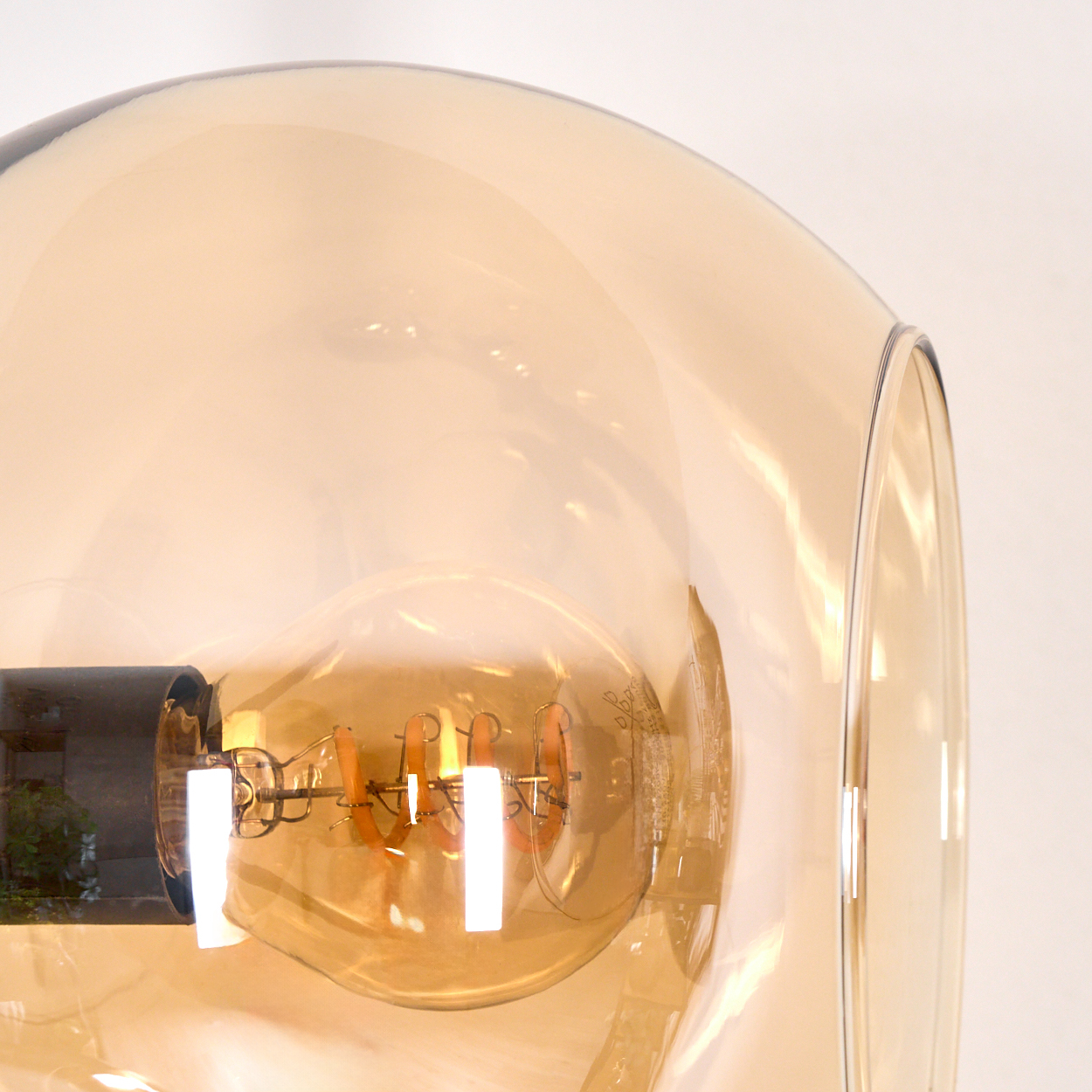 Nahaufnahme einer Glühbirne in einem Glasschirm. Die Glühfäden der Birne sind sichtbar, das Glas ist bernsteinfarben.
