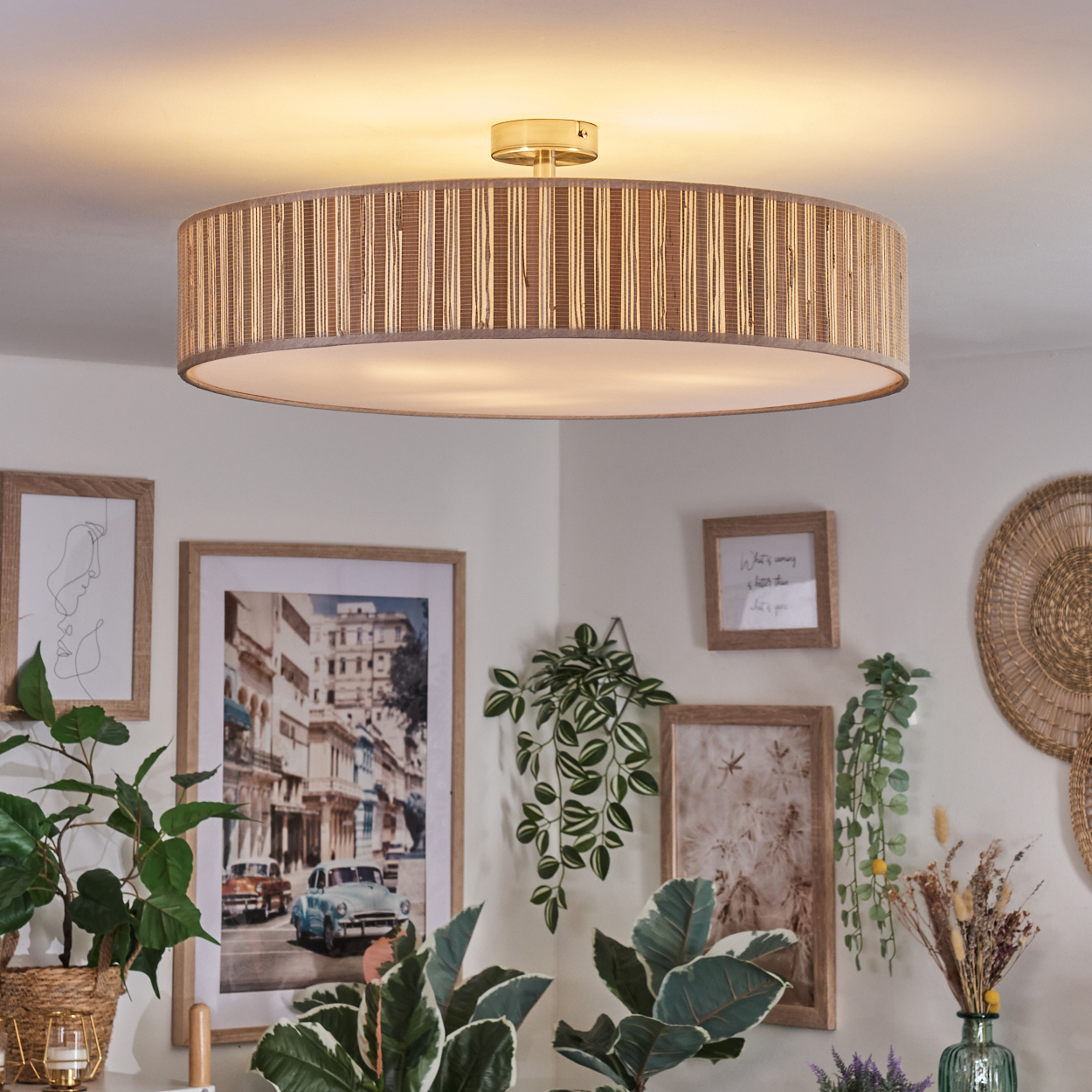 Eine dekorative Deckenlampe mit gewebtem Schirm ist zentriert. Gerahmte Kunstwerke und Pflanzen umgeben sie und schaffen eine gemütliche Atmosphäre.