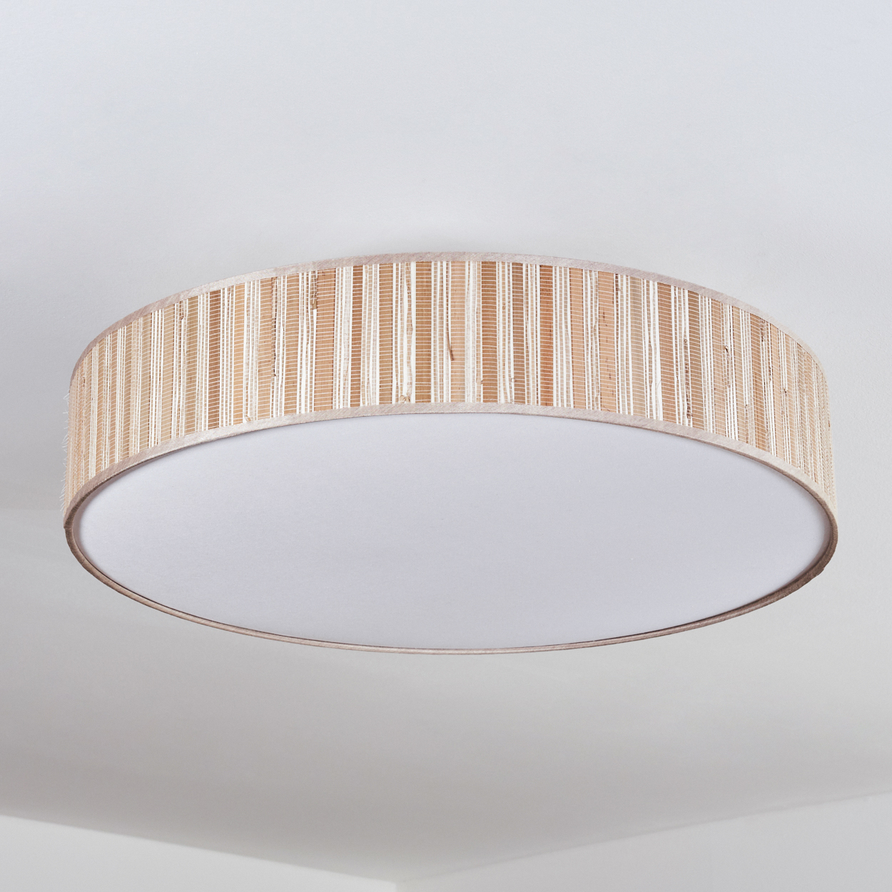 Eine runde Deckenleuchte mit gewebtem, beigem Schirm. Die Lampe hat einen weißen, kreisförmigen Diffusor und ist an einer weißen Decke montiert.