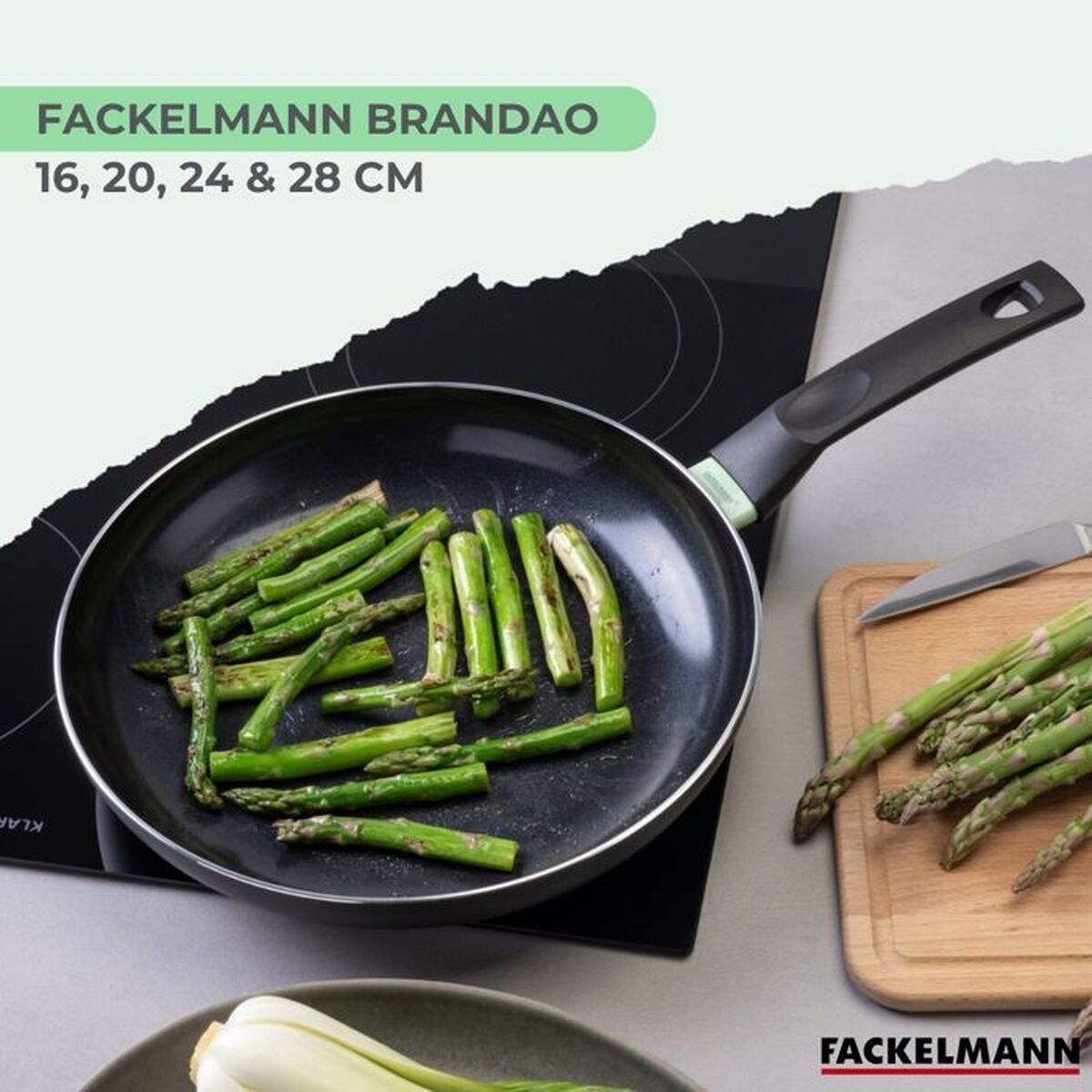 Eine Bratpfanne mit Spargel auf einem schwarzen Kochfeld, ein Schneidebrett mit Spargel und einem Messer.
