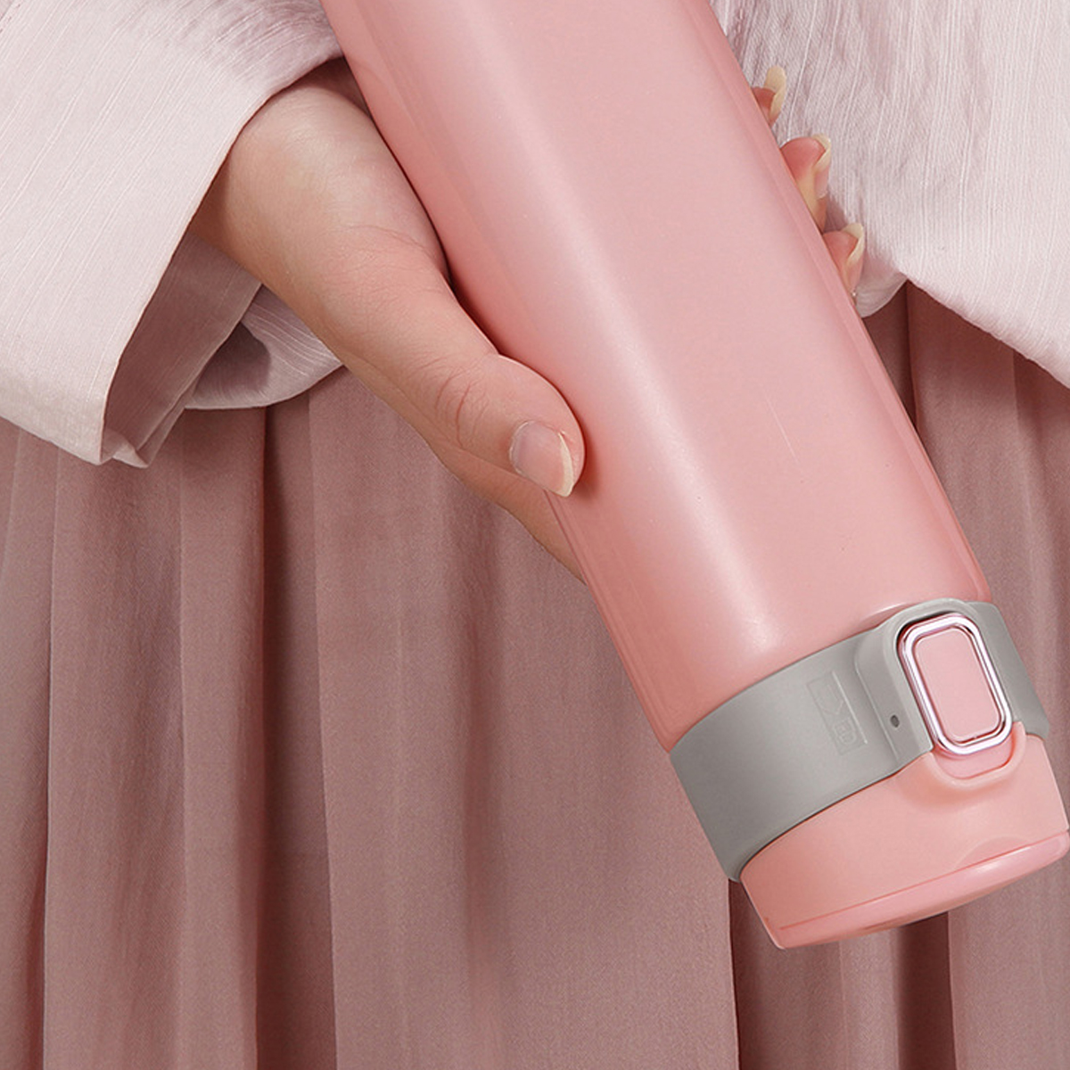 Eine Person hält eine rosa Wasserflasche. Die Flasche hat ein graues Band in der Nähe der Oberseite. Die Person trägt ein rosa Hemd und einen Rock.