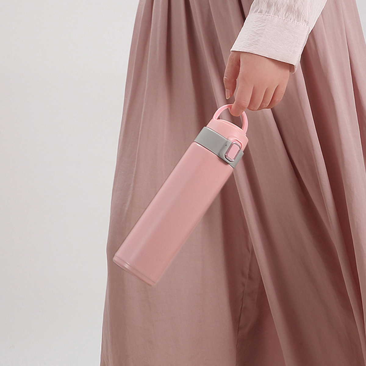 Eine Person hält eine rosa Wasserflasche. Die Person trägt ein weißes Hemd und einen rosa Rock. Der Hintergrund ist weiß.