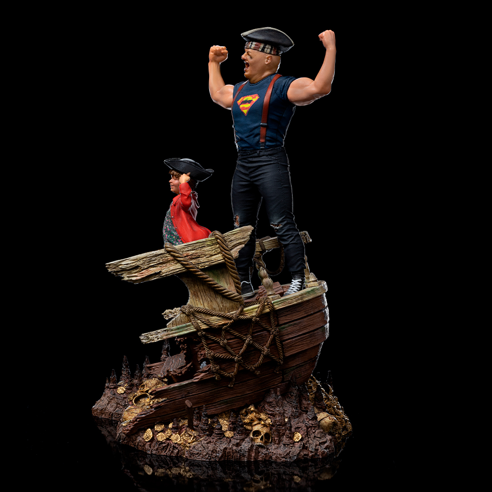 Statue eines Mannes mit erhobenen Armen, Piratenhut und Superman-Shirt. Kind im roten Mantel. Sie stehen auf einem Schiff mit Schatz.