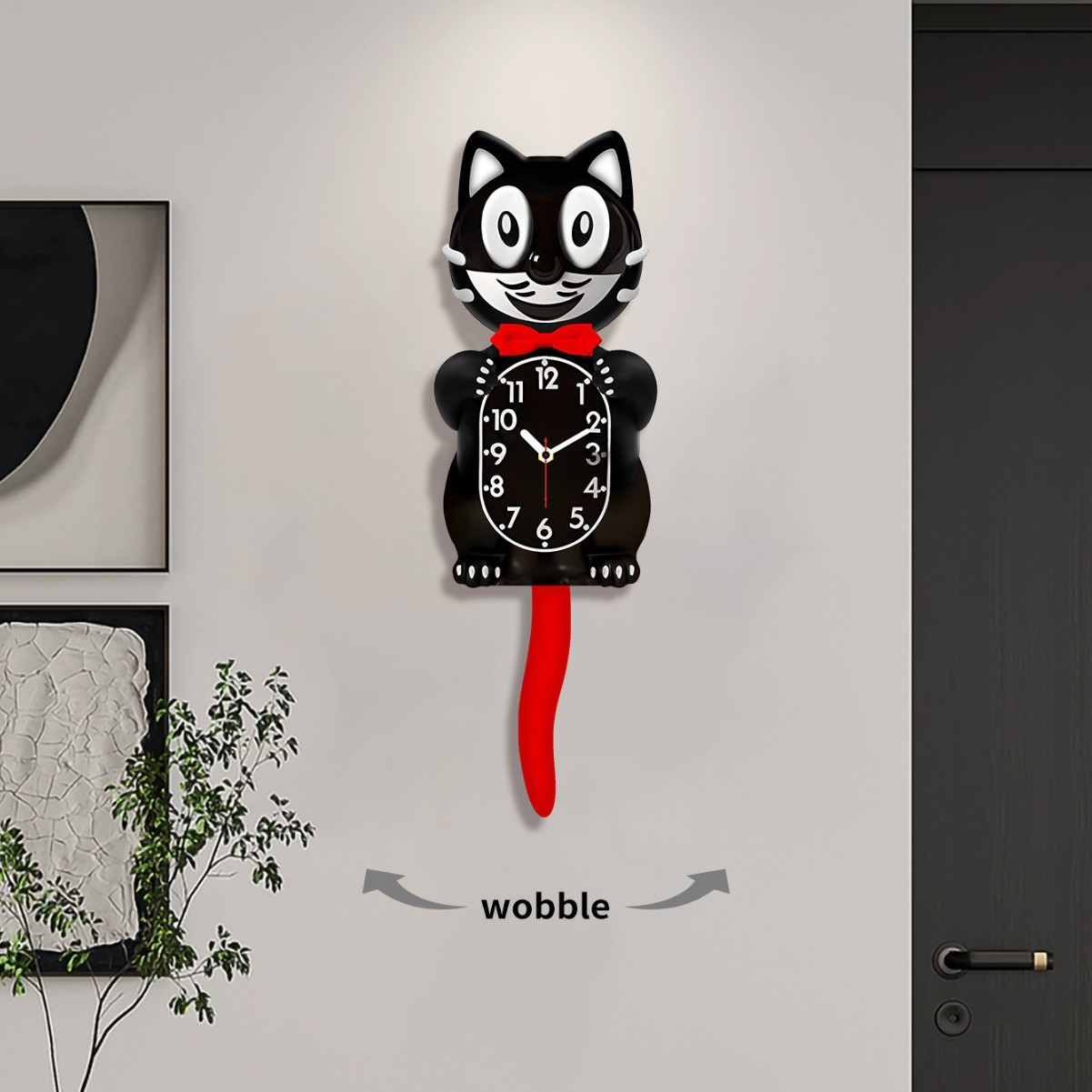 Eine katzenförmige Wanduhr mit roter Fliege und Schwanz, die an einer weißen Wand hängt. Der Schwanz wackelt. Schwarze und weiße Katzenuhr.