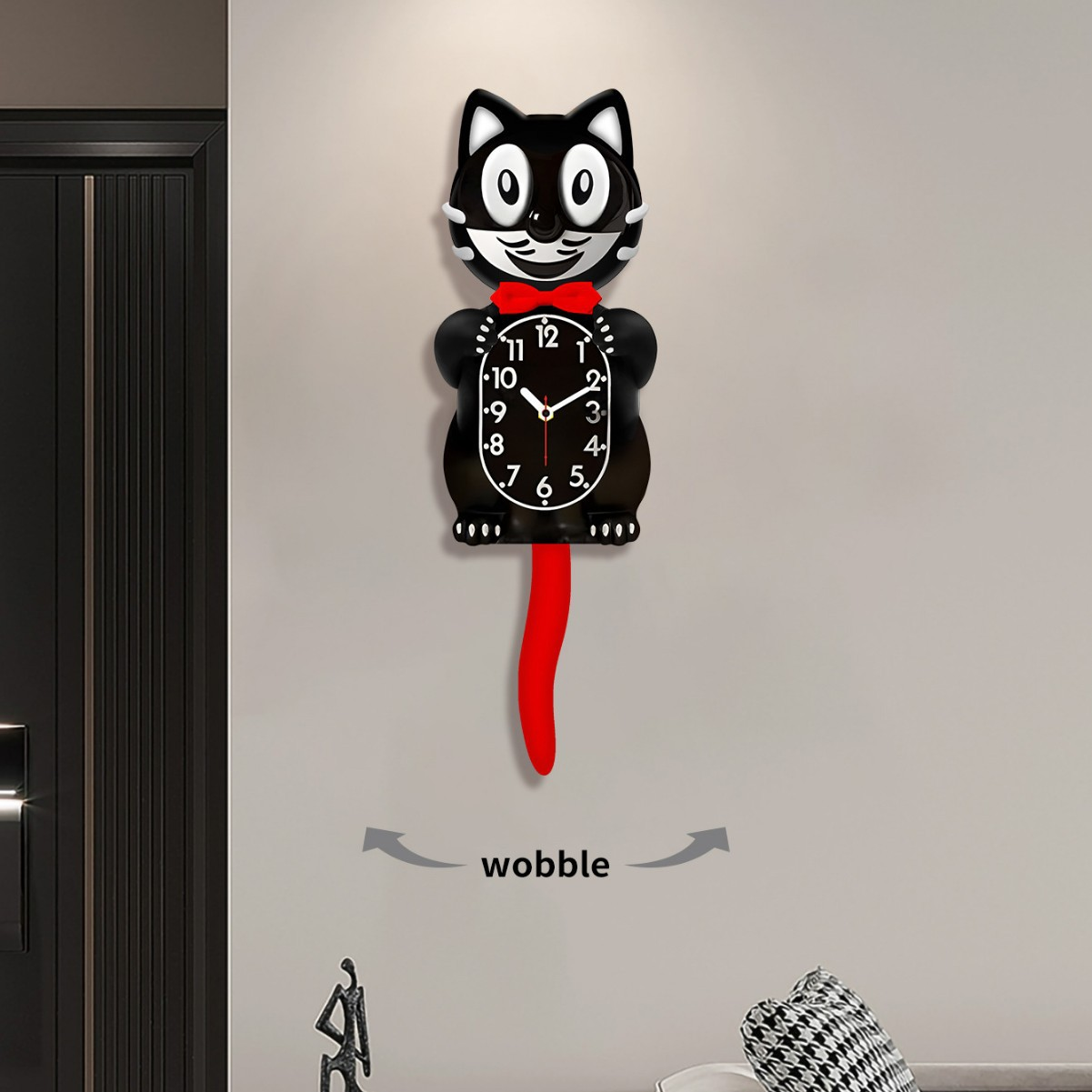 Eine schwarze Katzenuhr an der Wand, mit roter Fliege und Schwanz. Die Uhr zeigt 10:07. Darunter steht das Wort Wobble.