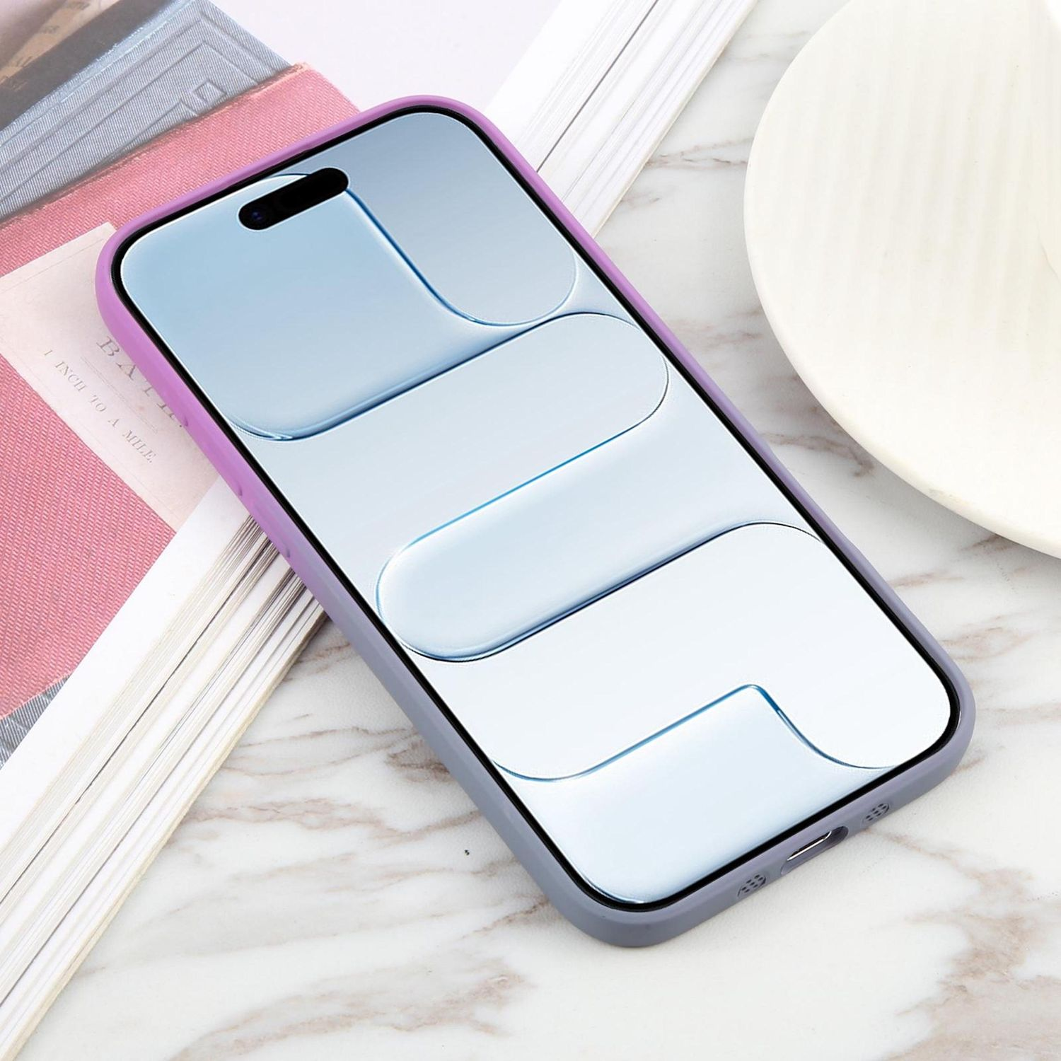 Un smartphone en una funda morada y gris descansa sobre un libro y una superficie de mármol, con un platillo blanco visible.