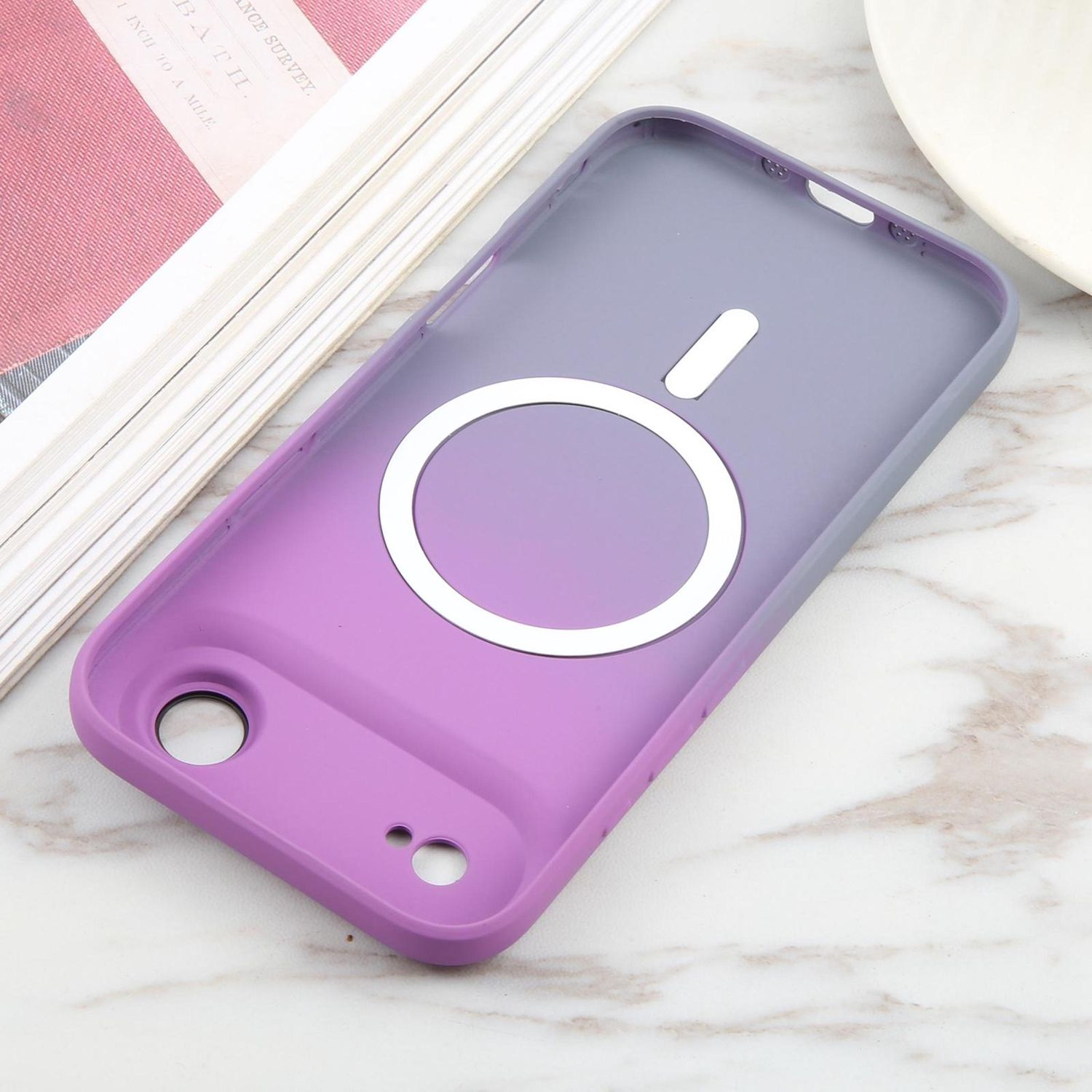 Una funda morada y gris con un diseño circular blanco. Descansa sobre una superficie de mármol, junto a un libro y un plato blanco.