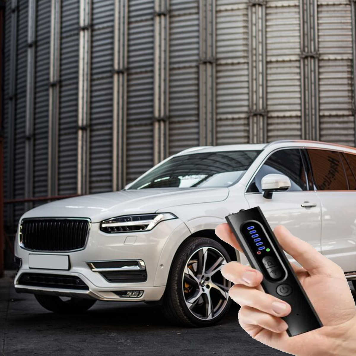 Eine Hand hält ein schwarzes Gerät vor einem weißen SUV. Im Hintergrund eine Metallstruktur.
