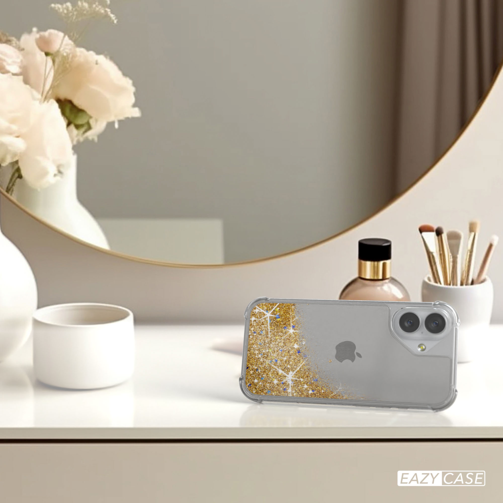 Ein Telefon in einer Hülle mit Goldglitter, Blumen in einer Vase, Make-up und ein runder Spiegel im Hintergrund.