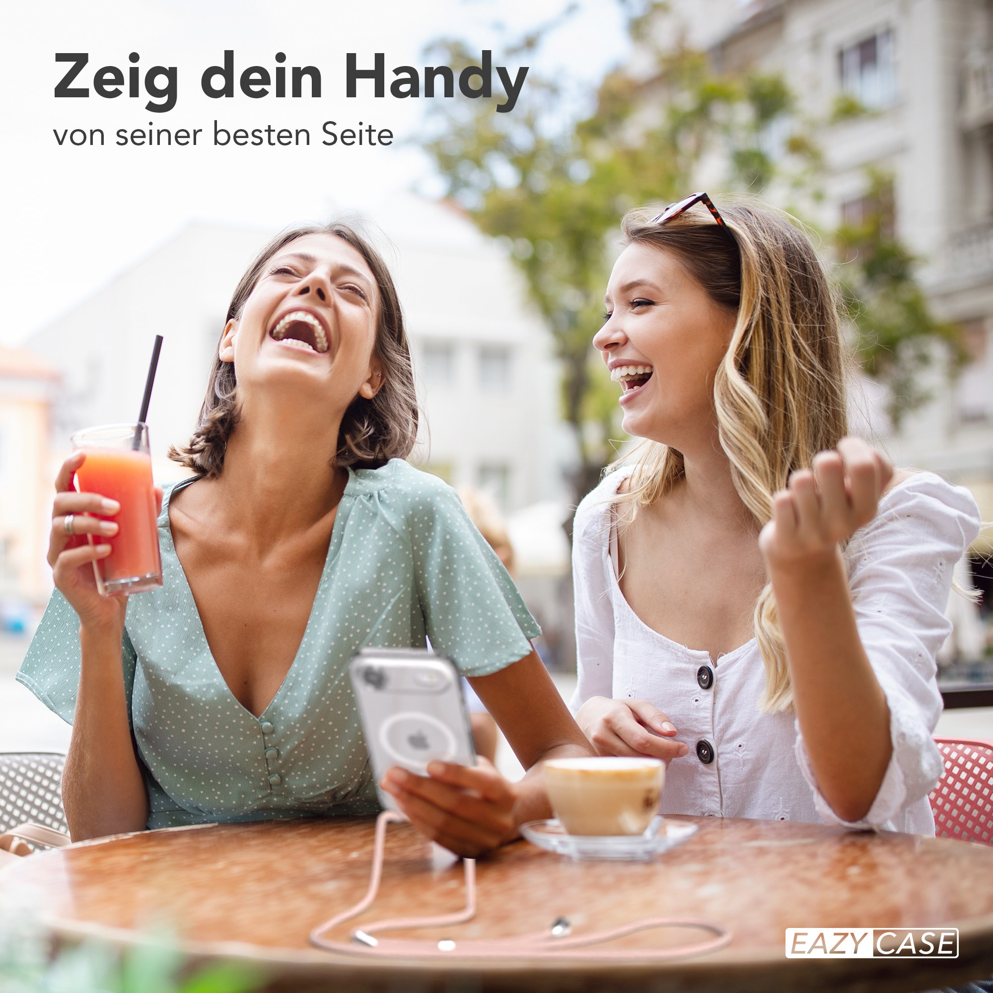 Zwei lachende Frauen in einem Café. Eine hält ein Telefon, die andere ein Getränk. Café-Einstellung mit Gebäuden im Hintergrund.