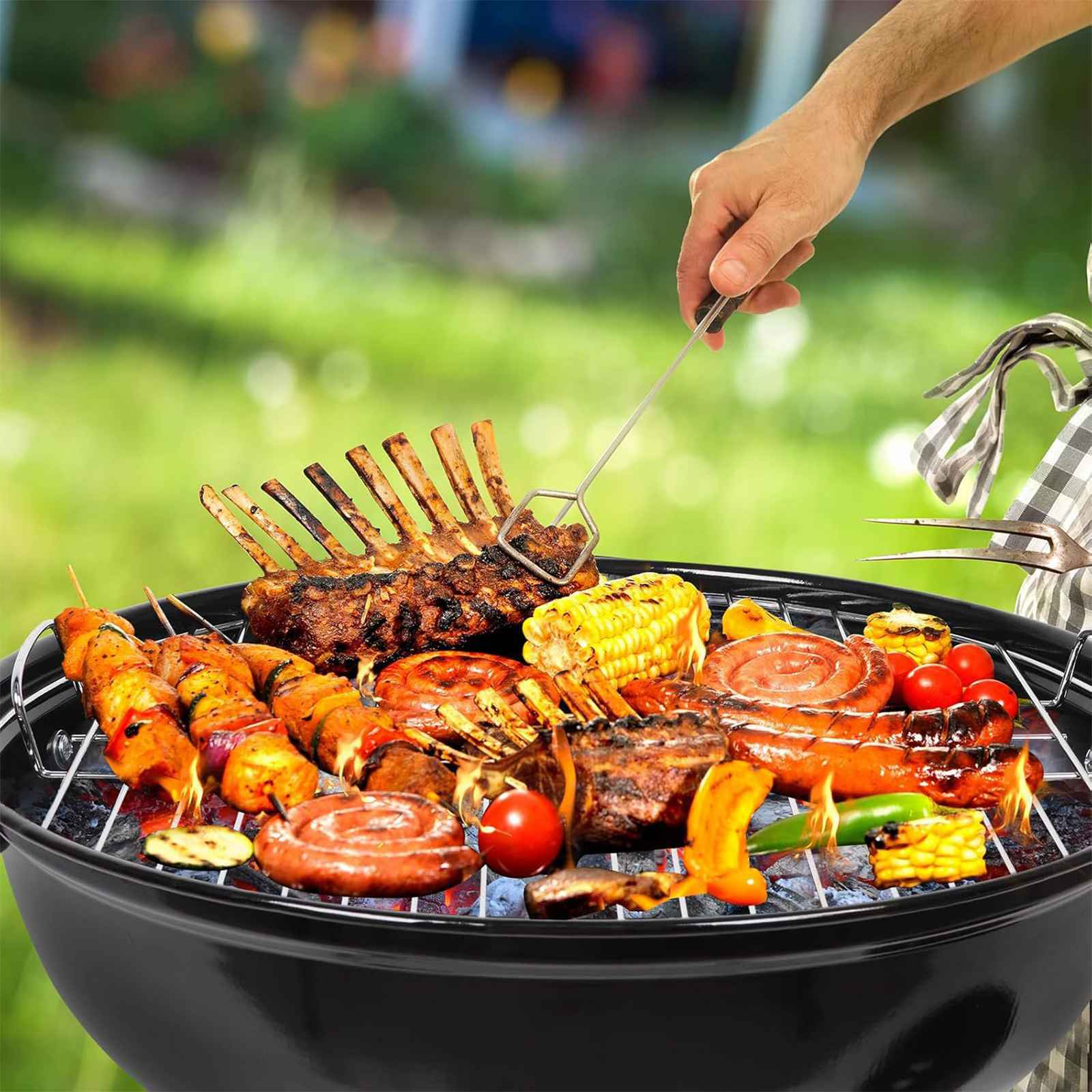 Grill mit verschiedenen Grillgerichten, darunter Spieße, Rippchen, Mais und Würstchen. Eine Hand hält ein Grillwerkzeug.