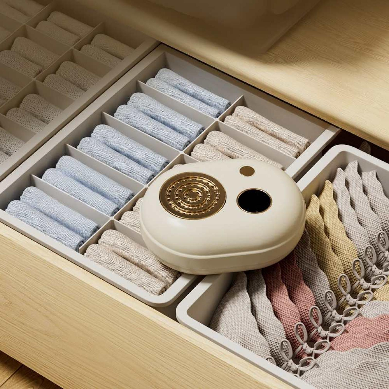 Eine Schublade mit organisierten Fächern. Gerollte Handtücher in verschiedenen Farben sind ordentlich angeordnet. Ein cremefarbener Aromadiffusor liegt in der Mitte.