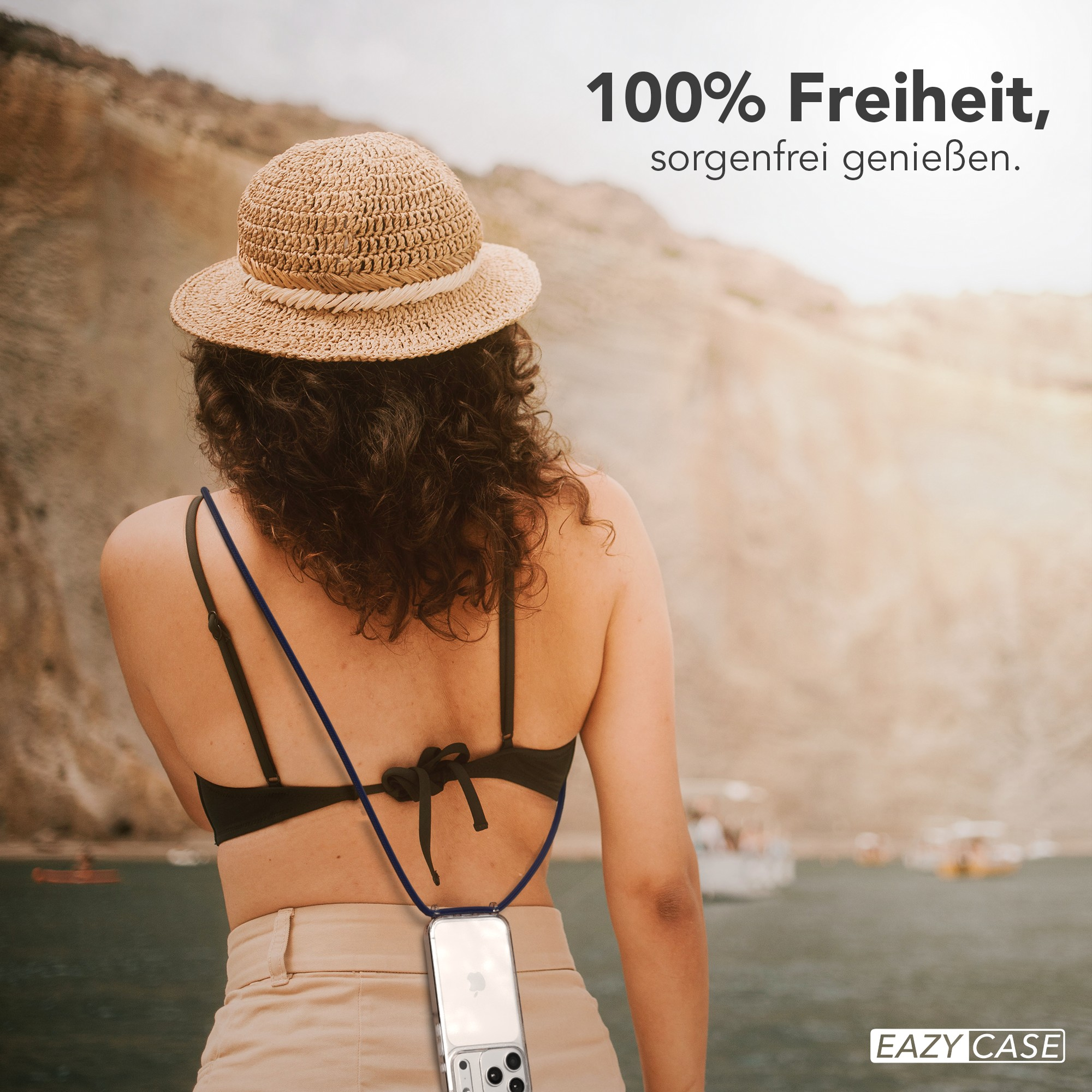 Frau mit Hut, schwarzem Oberteil, beiger Hose, Telefon an einem Schlüsselband, Berge im Hintergrund, Text '100% Freiheit'.