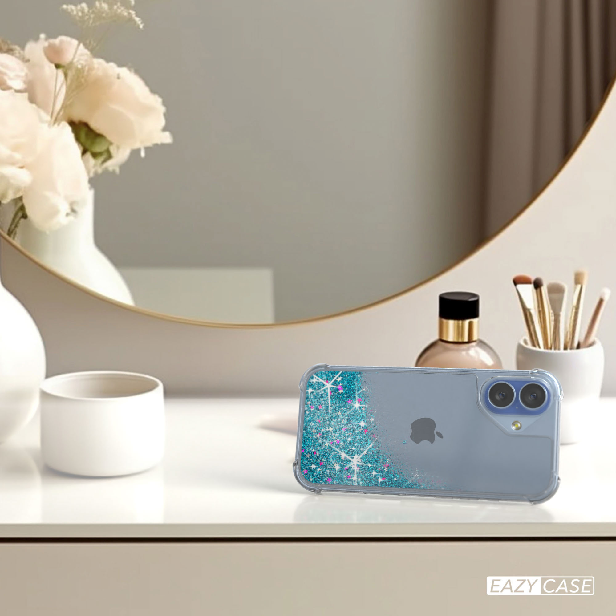 Eine Handyhülle mit blauem und Glitzerdesign auf weißer Oberfläche, mit Blumen und Spiegel im Hintergrund.