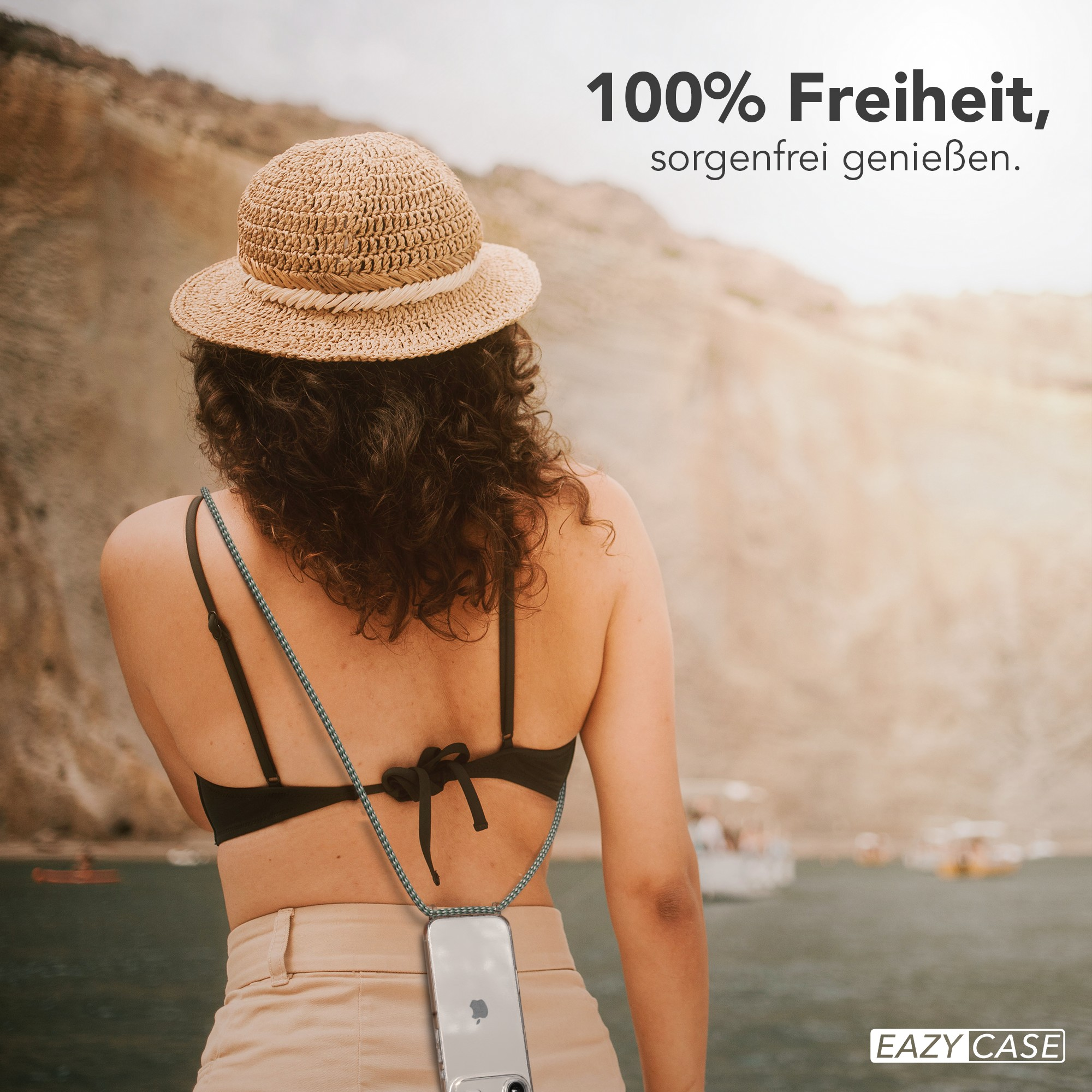 Frau mit Strohhut und Handyhülle, abgewandt, vor Meer und Bergen.