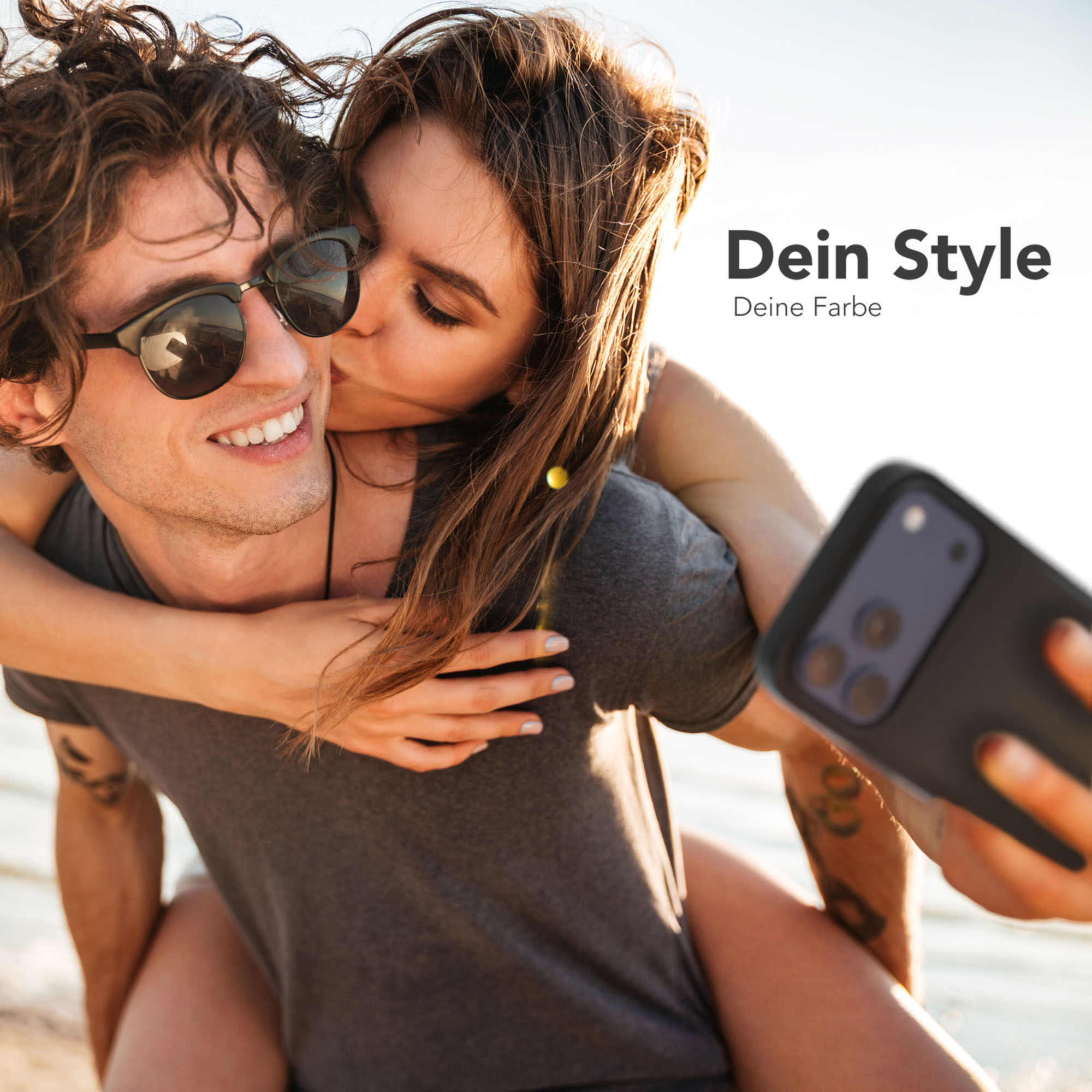 Ein Mann trägt eine Frau Huckepack, beide lächeln. Die Frau küsst die Wange des Mannes. Sie machen ein Selfie.