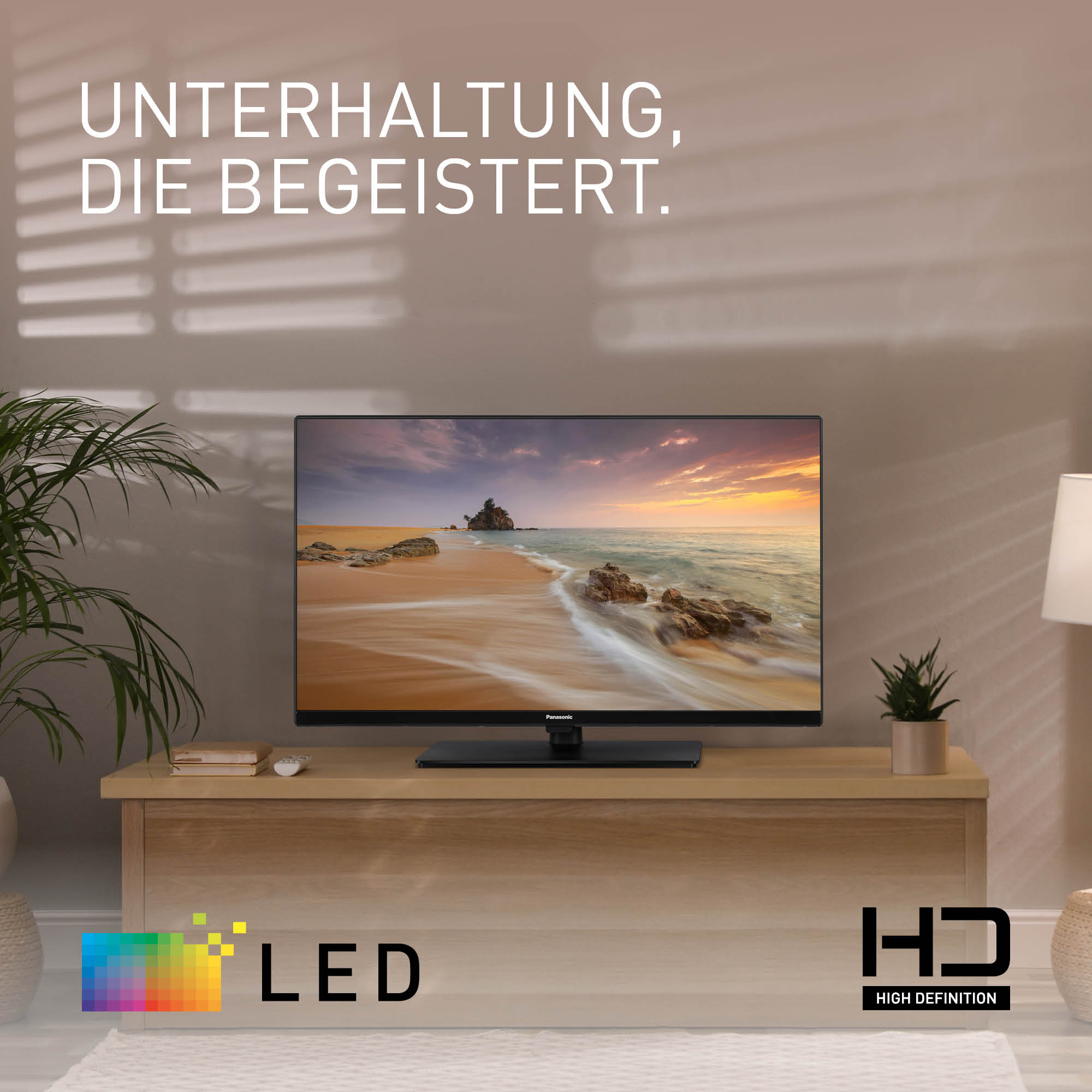 Una TV su un supporto in legno mostra una scena di spiaggia. Il testo in alto dice 'Intrattenimento che ispira'.