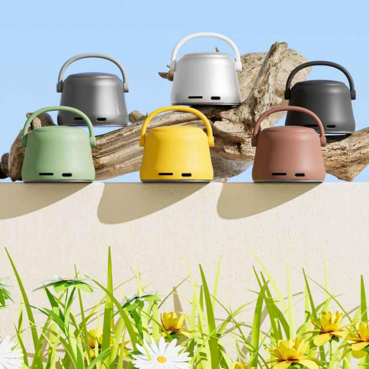 Sechs bunte, eimerförmige Geräte mit Griffen sind auf einer strukturierten Oberfläche angeordnet, über Gras und Blumen. Der Hintergrund ist blau.