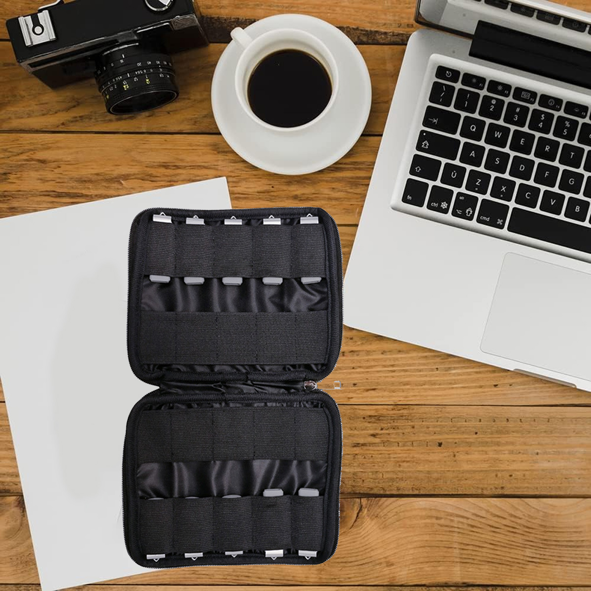 Draufsicht auf einen Schreibtisch mit Laptop, Kamera, Kaffeetasse, offenem Organizer und Papier auf Holzoberfläche.