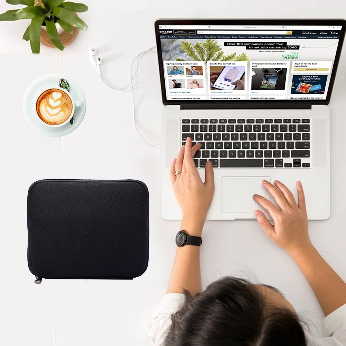 Eine Person benutzt einen Laptop. Eine Kaffeetasse, eine schwarze Hülle und Kopfhörer liegen auf dem Tisch. Der Laptop zeigt eine Amazon-Webseite.