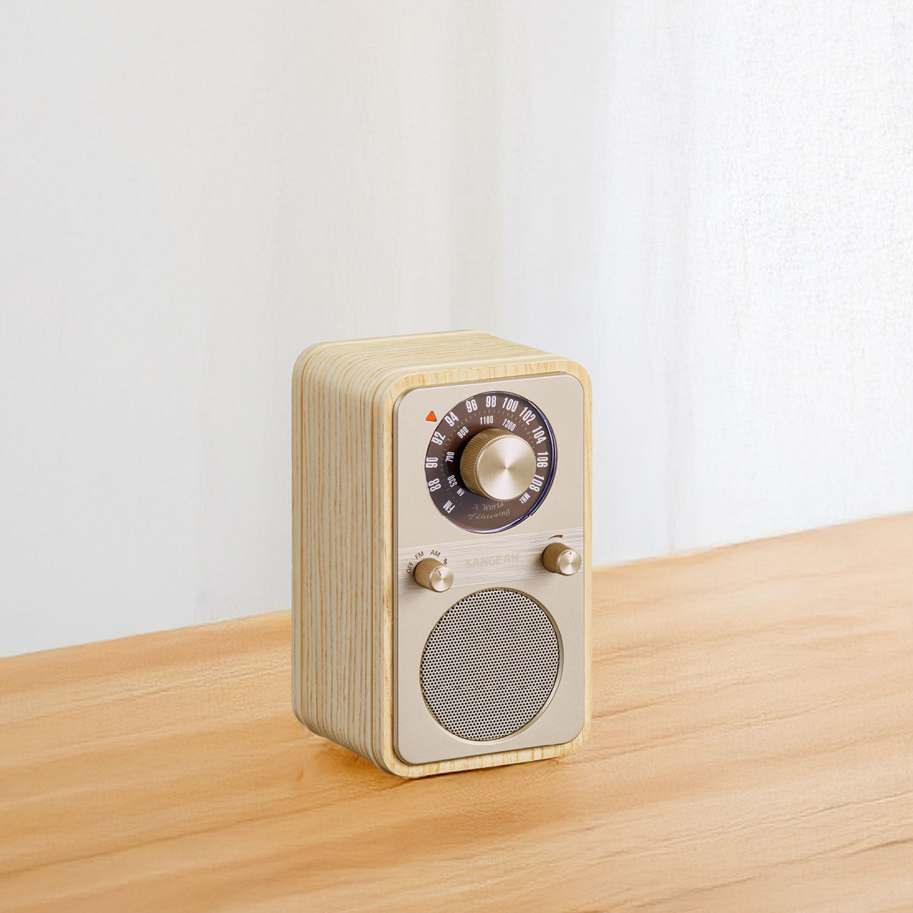 Ein Holzradio steht auf einer Holzoberfläche. Das Radio hat einen Lautsprecher, Knöpfe und einen Abstimmknopf. Der Hintergrund ist weiß.