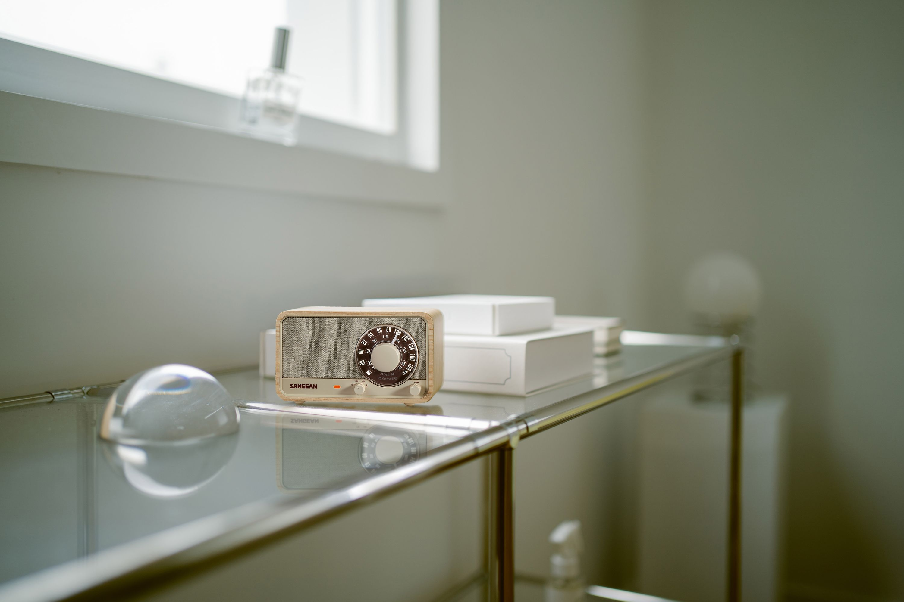 Ein Holzradio steht mit Büchern auf einem Glasregal. Eine klare Kuppel und eine Parfümflasche sind in der Nähe.