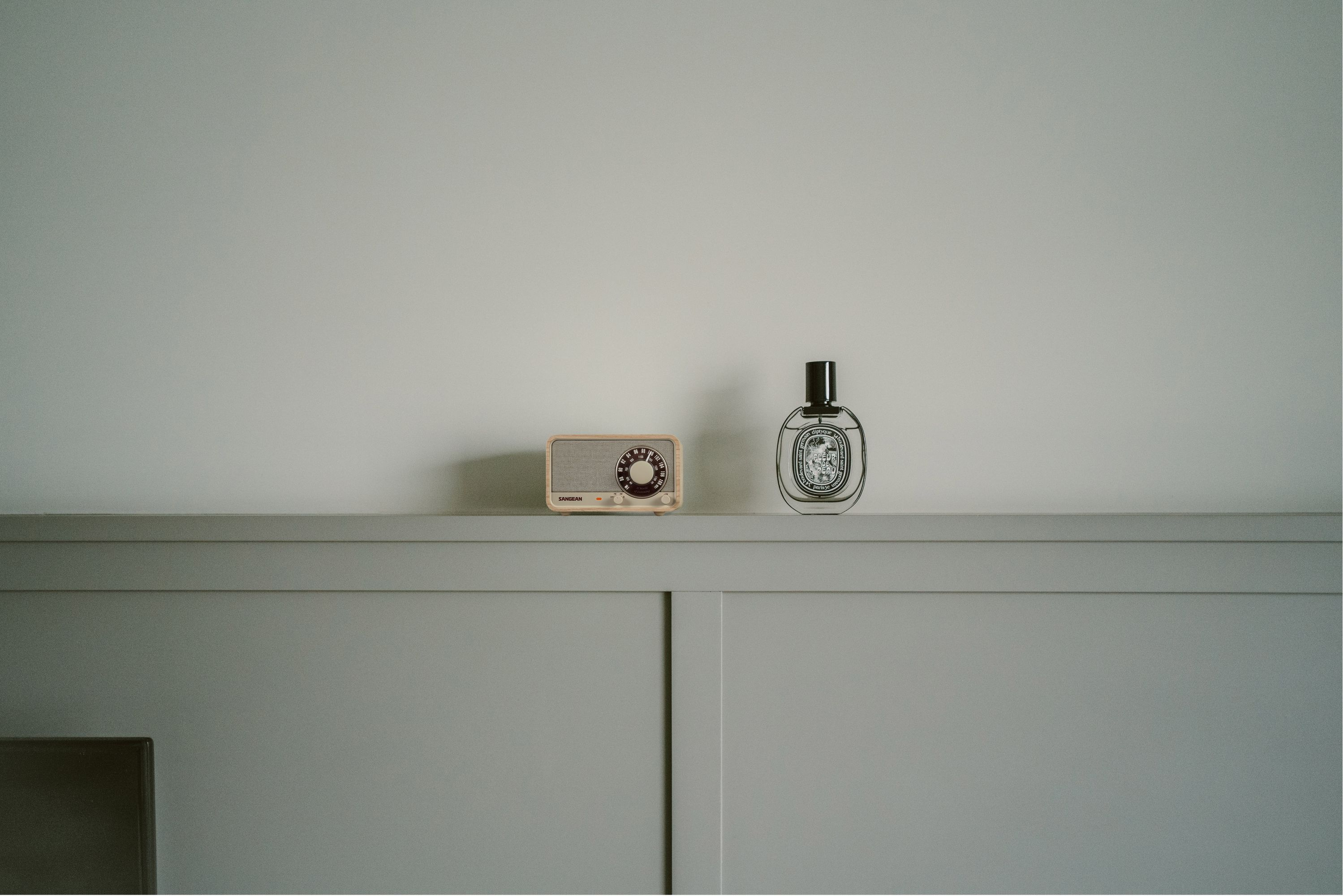 Ein Radio und eine Parfümflasche stehen auf einer grauen Oberfläche vor einer weißen Wand.