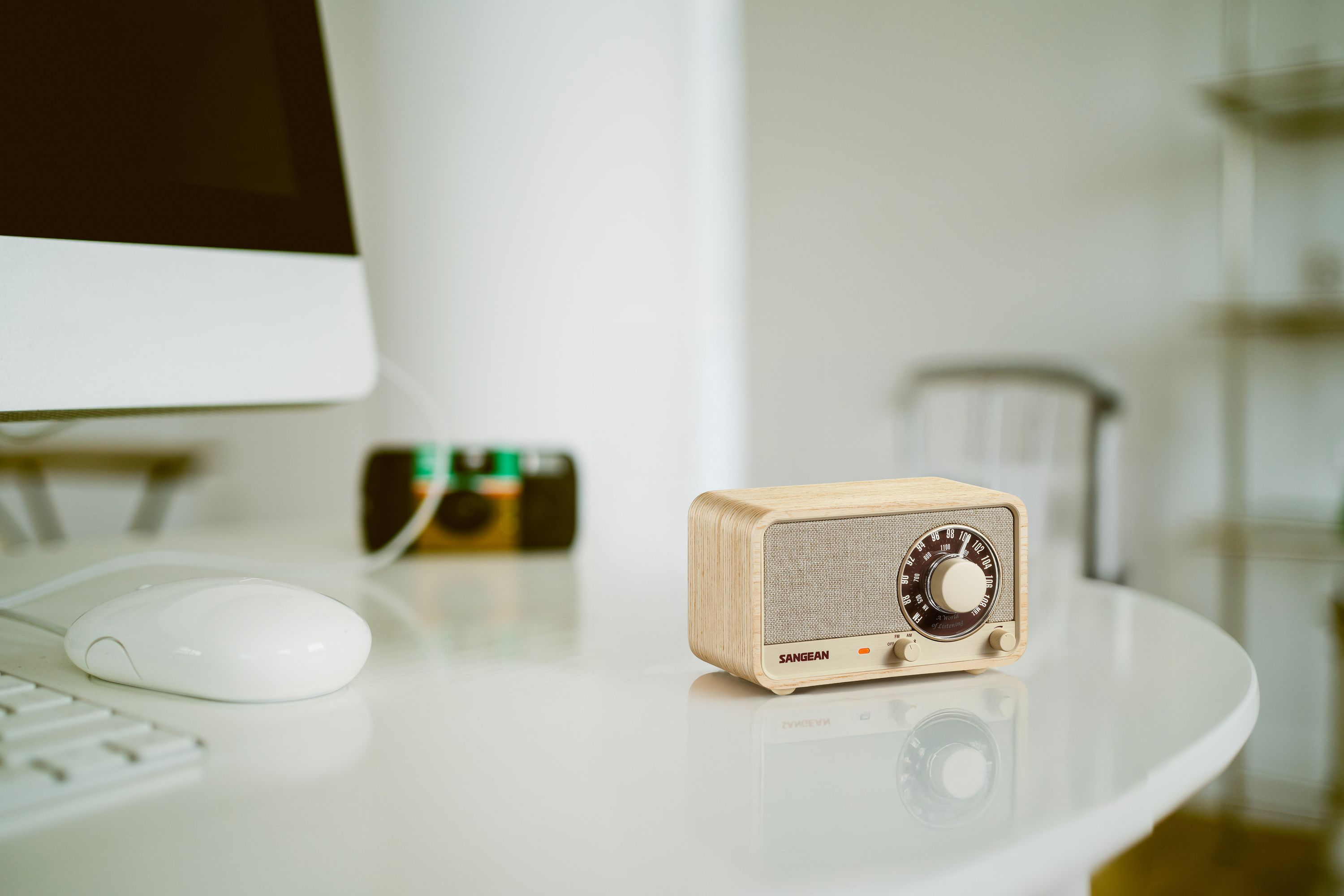 Ein Holzradio steht auf einem weißen Schreibtisch mit Computer und Maus. Eine Kamera ist im Hintergrund.