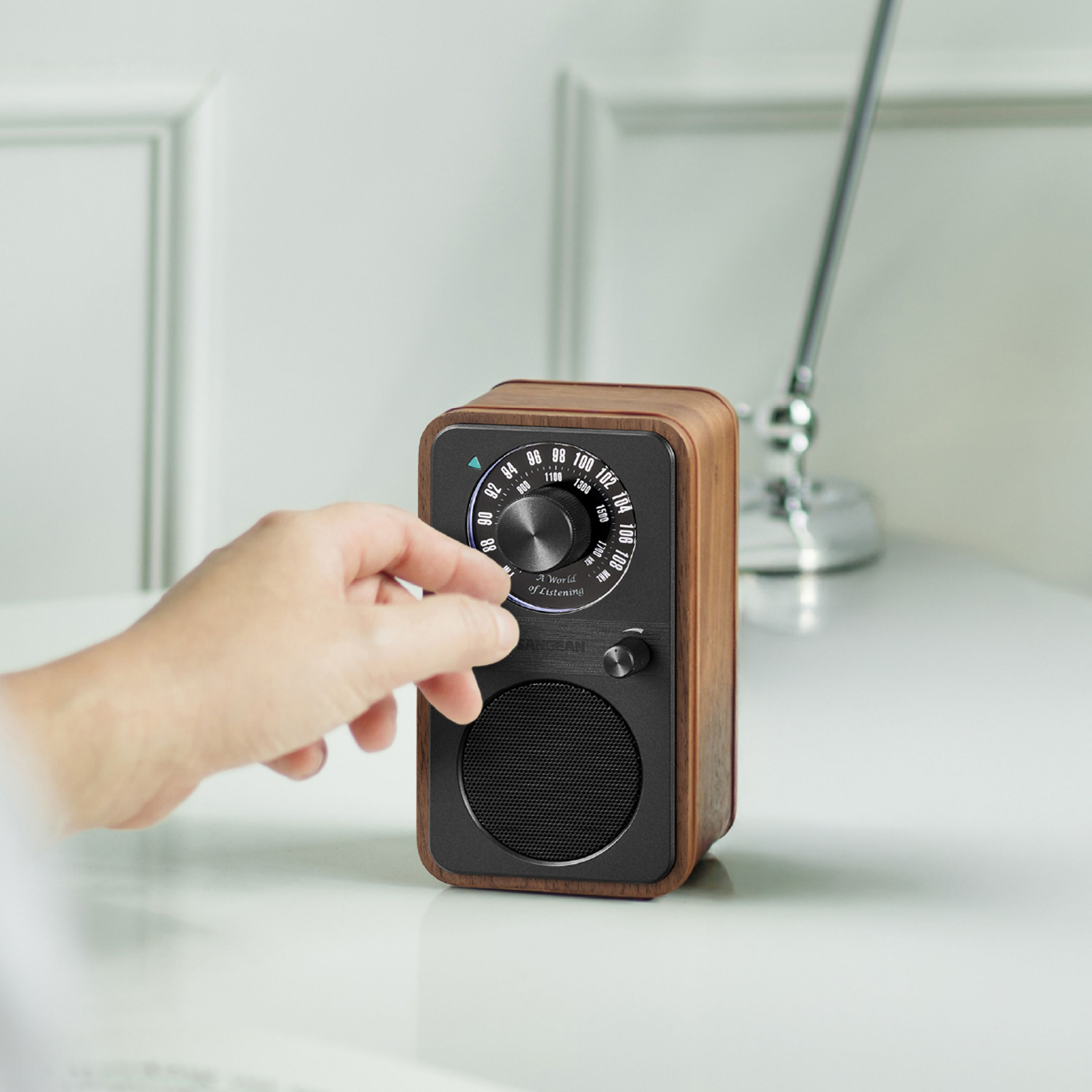 Eine Hand stellt ein Holzradio mit schwarzer Front ein. Das Radio steht auf einer weißen Oberfläche.