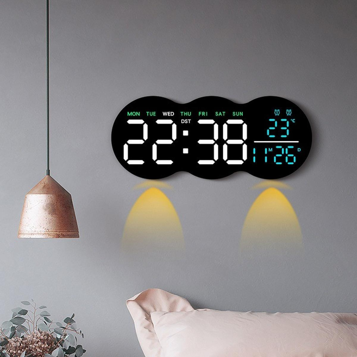Eine Digitaluhr an einer grauen Wand zeigt Zeit, Datum und Temperatur. Eine Hängelampe und ein Kissen sind zu sehen.