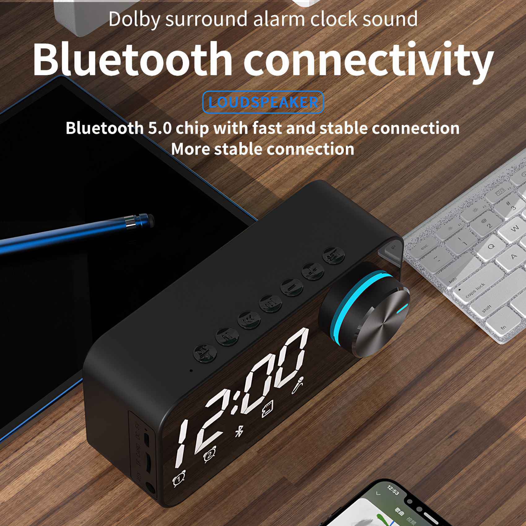 Schwarzer Bluetooth-Lautsprecher mit Digitaluhr auf Holzoberfläche, neben Tablet und Tastatur.