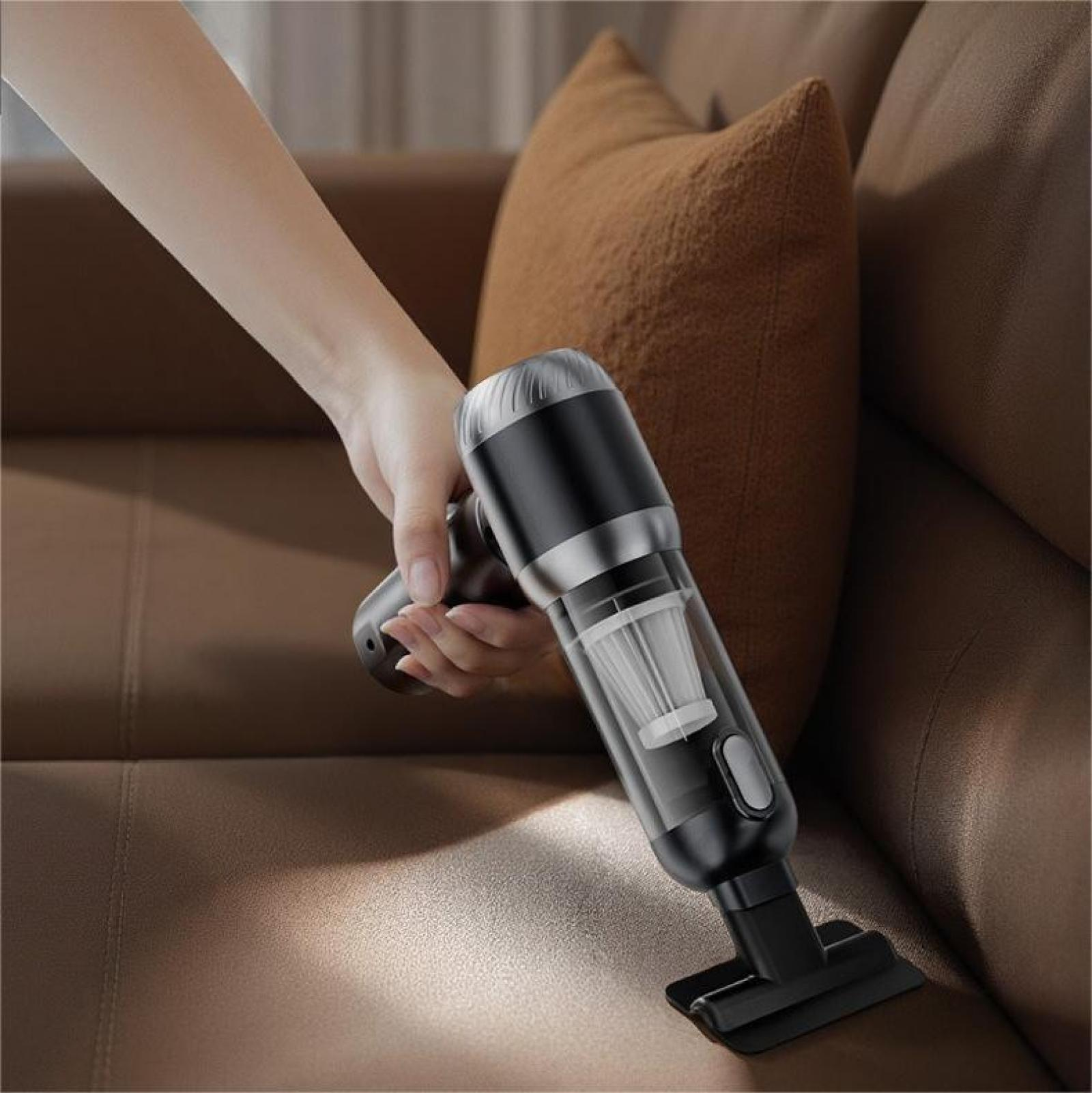 Hand hält einen schwarzen und silbernen Handstaubsauger und reinigt ein braunes Ledersofa. Im Hintergrund ist ein braunes Kissen.