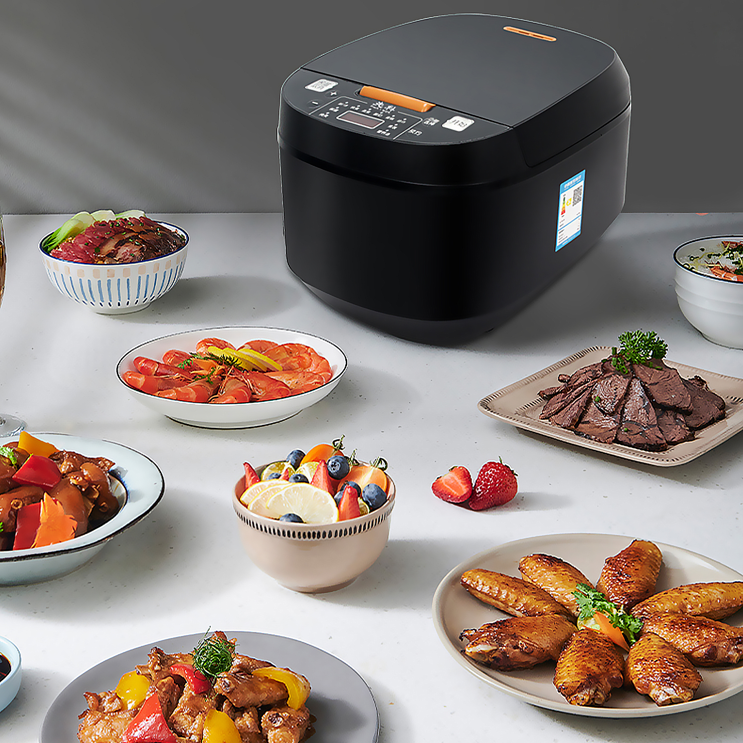 Una cuociriso nera è tra vari piatti: gamberi, frutta, carne e ali di pollo. È preparata una tavola per un pasto.