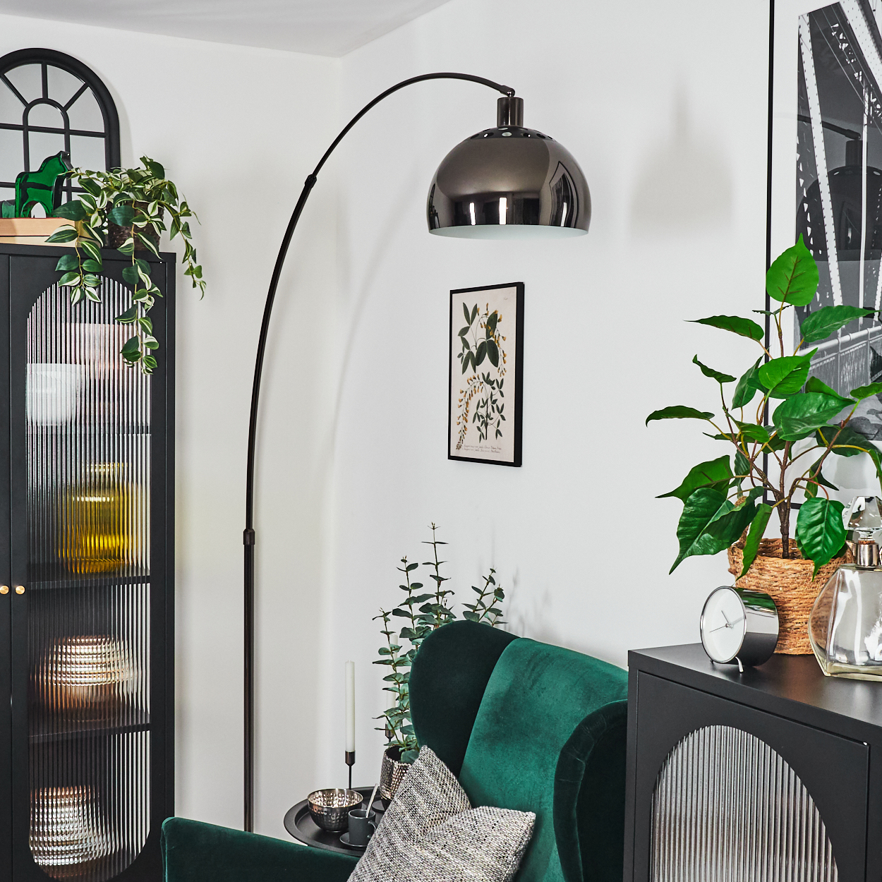 Ein modernes Wohnzimmer mit grünem Samt-Sessel, schwarzem Schrank, hoher Lampe und verschiedenen Pflanzen.