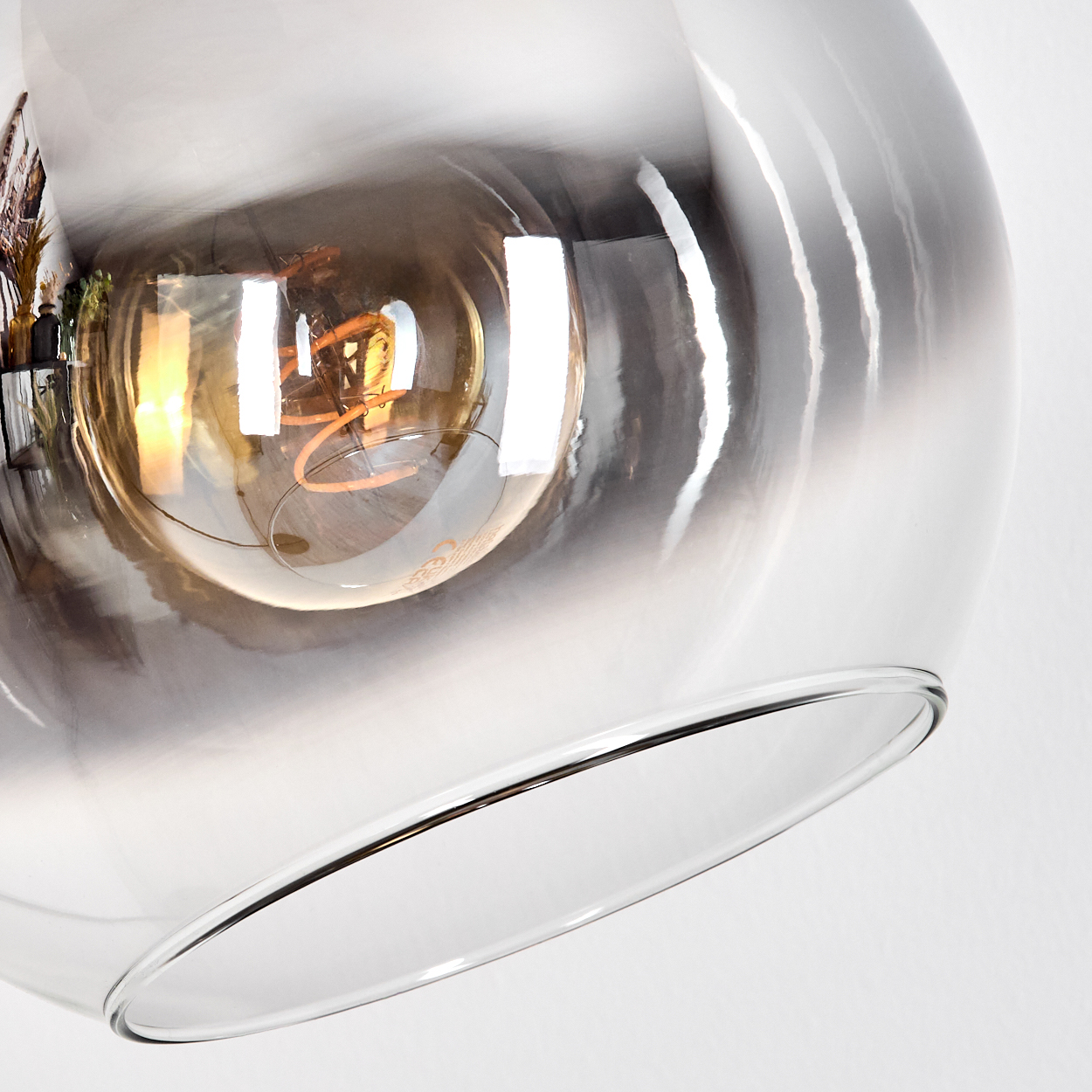 Nahaufnahme einer Glasleuchte mit sichtbarer Glühbirne. Das Glas hat einen Farbverlauf und befindet sich vor einem weißen Hintergrund.