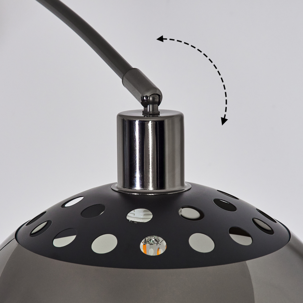Nahaufnahme einer Lampe mit schwarzem Schirm und silbernem Metallständer. Der Schirm hat Löcher und die Lampe ist eingeschaltet.