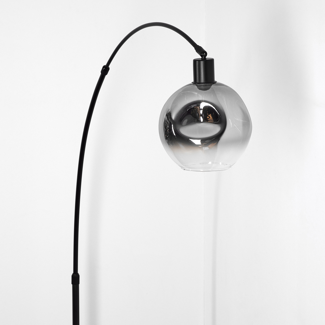 Eine moderne schwarze Lampe mit gebogenem Arm und einem Glasschirm. Der Schirm hat einen Farbverlauf. Der Hintergrund ist weiß.