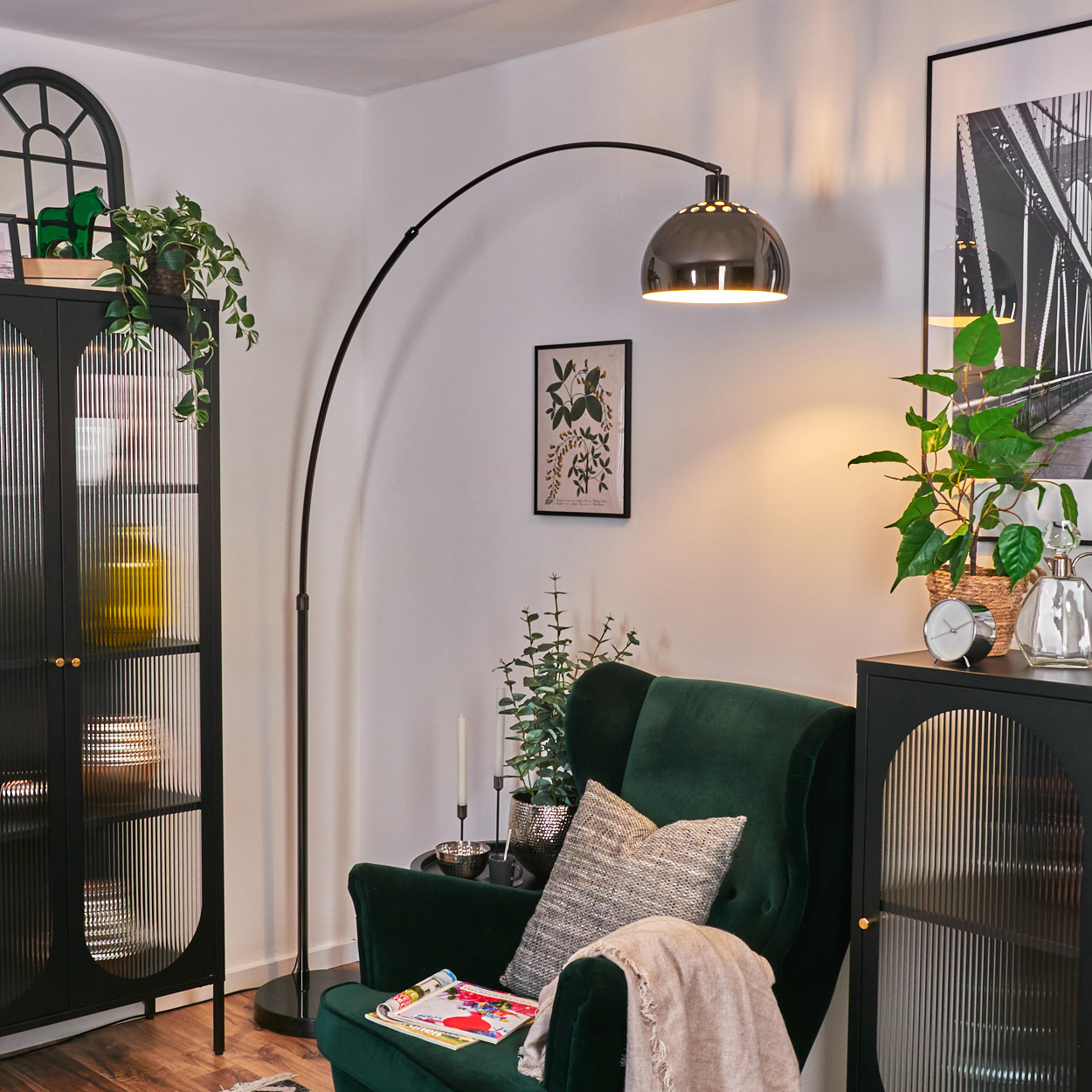 Ein Wohnzimmer mit grünem Sessel, Stehlampe und schwarzem Schrank mit Pflanzen und Dekorationen.