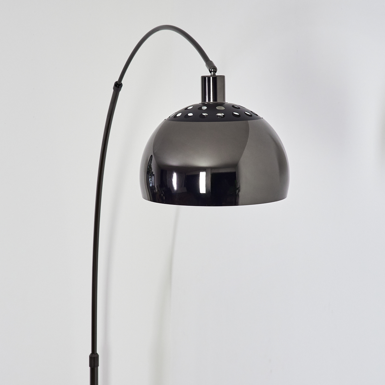 Eine moderne, metallische Stehlampe mit gebogenem Arm und einem kuppelförmigen Schirm. Der Hintergrund ist eine schlichte, weiße Wand.