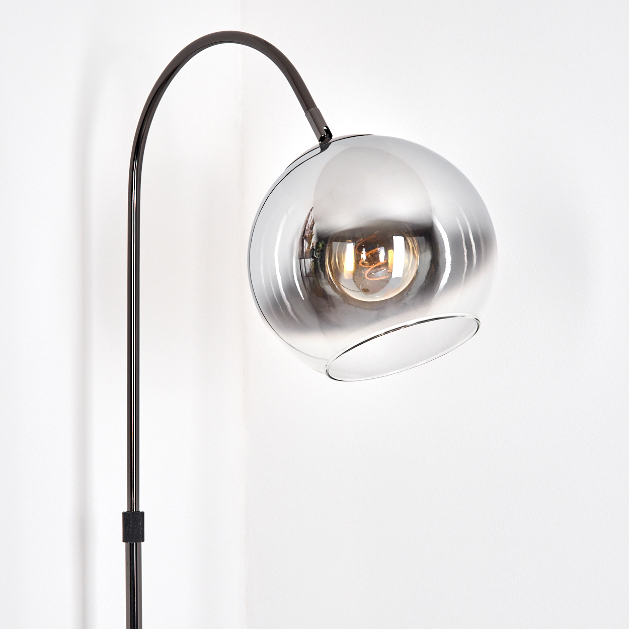Eine moderne Stehlampe mit schwarzem, gebogenem Arm und einem kugelförmigen, rauchfarbenen Glasschirm. Im Schirm ist eine Glühbirne sichtbar.