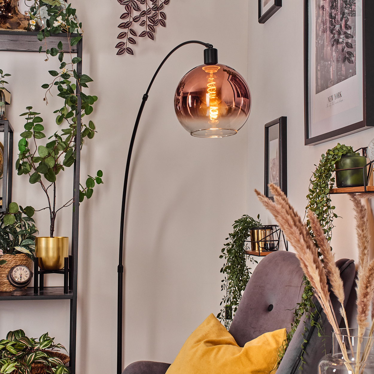 Ein Raum mit einer schwarzen Stehlampe mit rundem Glasschirm. Ein grauer Sessel mit gelbem Kissen. Pflanzen und Bilder im Hintergrund.