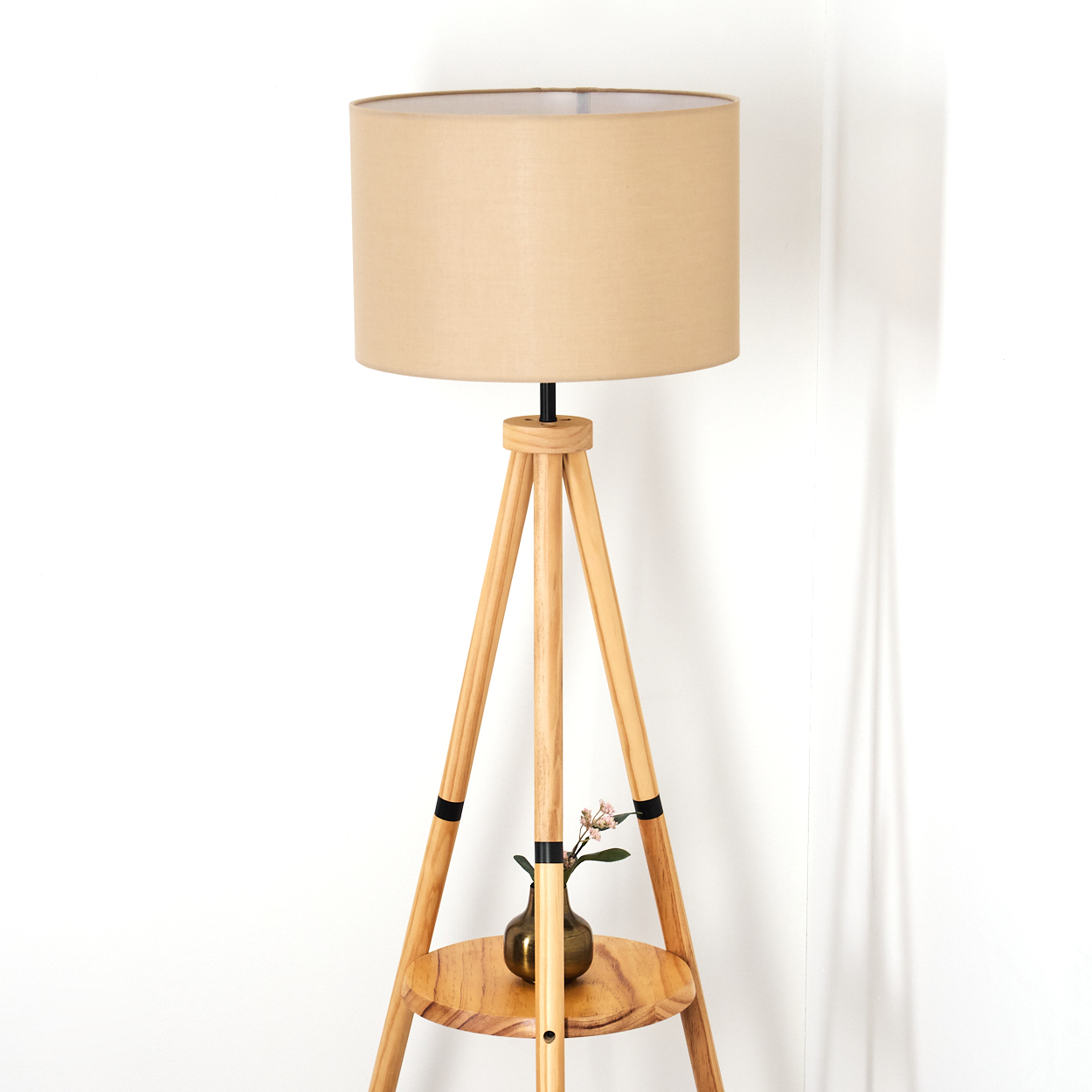 Ein beigefarbener Lampenschirm sitzt auf einer Stehlampe aus Holz. Eine kleine Vase mit Blumen steht auf einem Holzregal.
