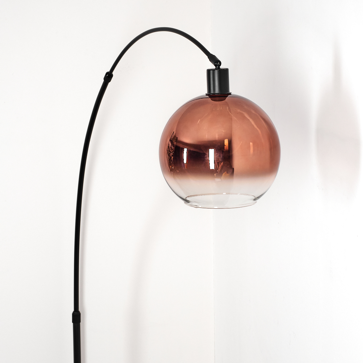 Eine moderne schwarze Stehlampe mit kugelförmigem, farbigem Glasschirm vor weißer Wand.