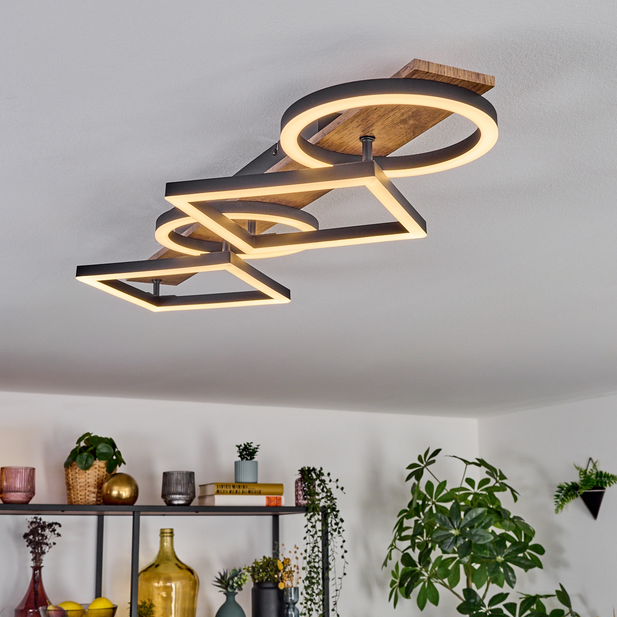Moderne Deckenleuchte mit geometrischen Formen. Darunter ein Regal mit Pflanzen und Dekoration. Helles, minimalistisches Innendesign.