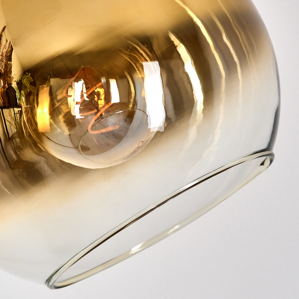 Nahaufnahme einer Glasleuchte, in der sich eine Glühbirne befindet. Das Glas ist bernsteinfarben, mit Metallrand und weißem Hintergrund.