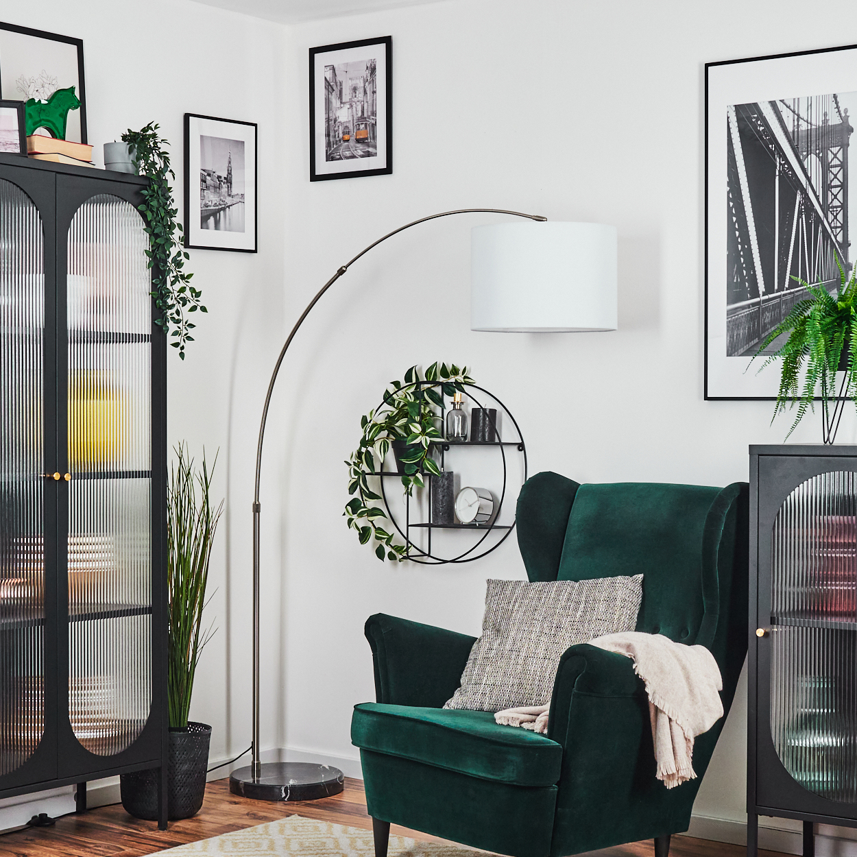 Ein grüner Sessel mit Decke und Kissen. Eine Stehlampe und ein schwarzer Schrank stehen daneben. Bilder hängen an der Wand.