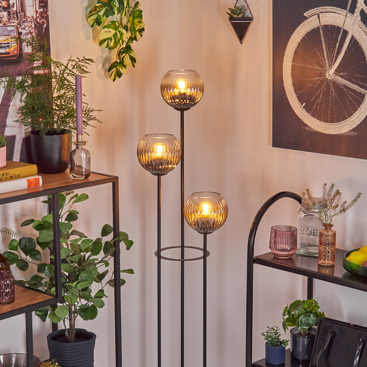 Raumecke mit Stehlampe, Regalen mit Pflanzen und Deko sowie Fahrradrad-Kunstwerk.